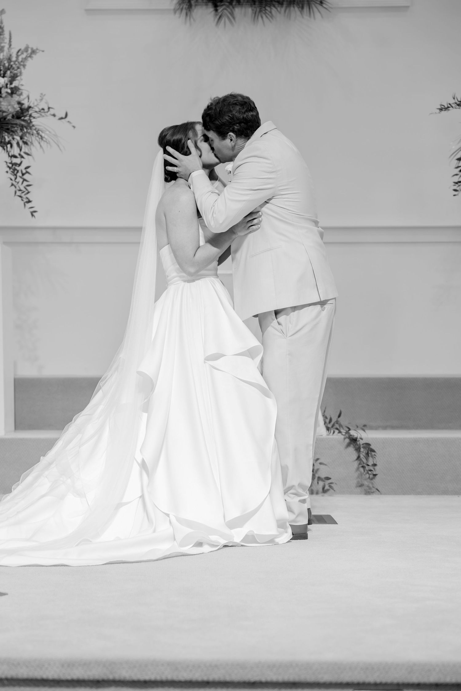 Black and white photo of bride and groom sharing their first kiss at the wedding altar.