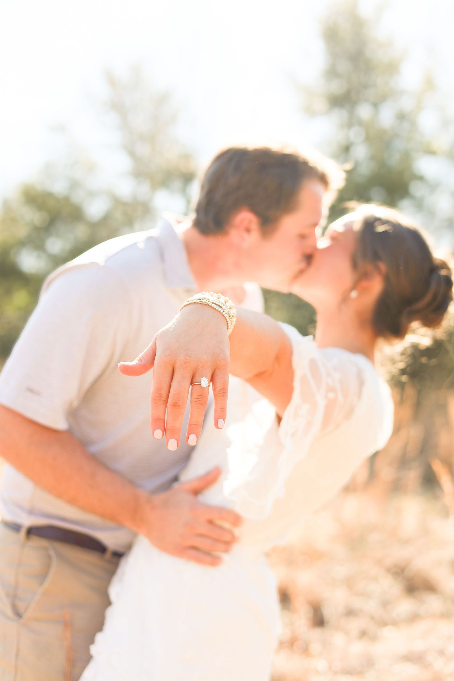 A romantic couple embraces outdoors in soft golden sunlight during a photo session.