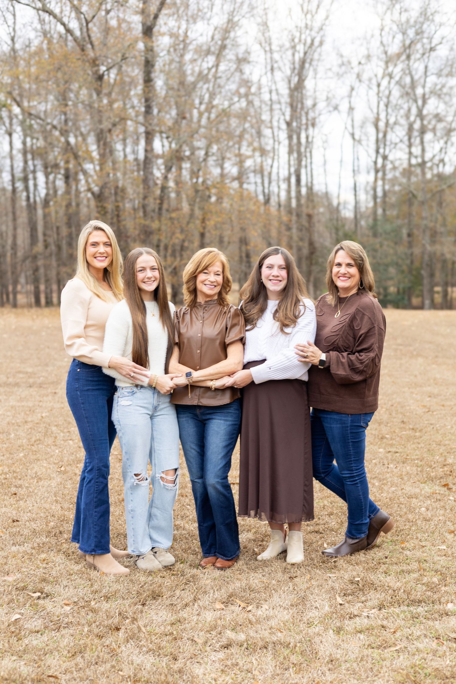 Group wearing matching brown tops and blue jeans pose creatively in a fall field with bare trees in background.