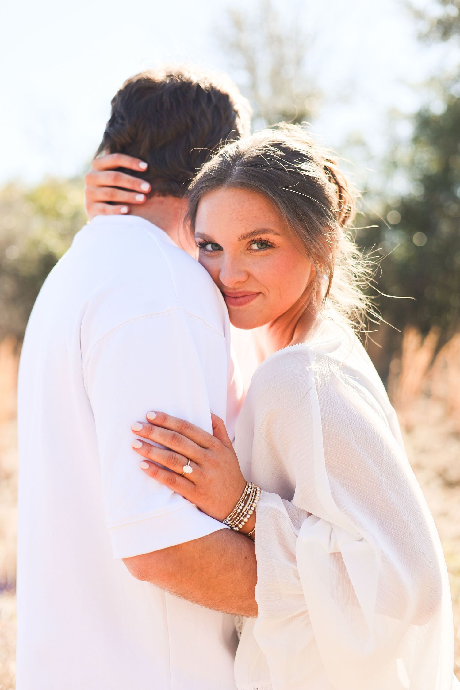 Romantic couple in white clothing embrace during outdoor photo session at sunset.