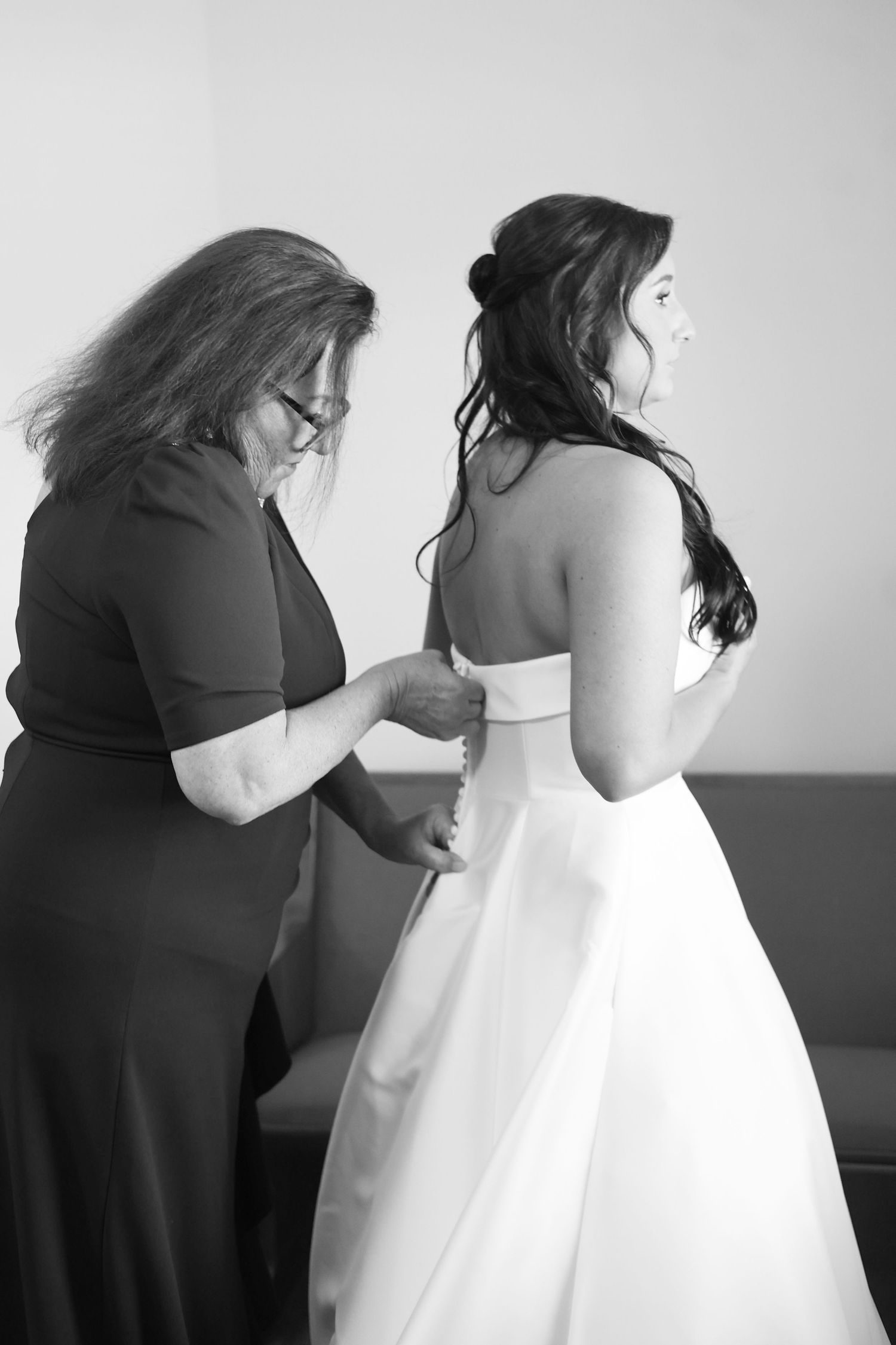A wedding dress fitting session shows someone making final adjustments to a white bridal gown in a studio setting.