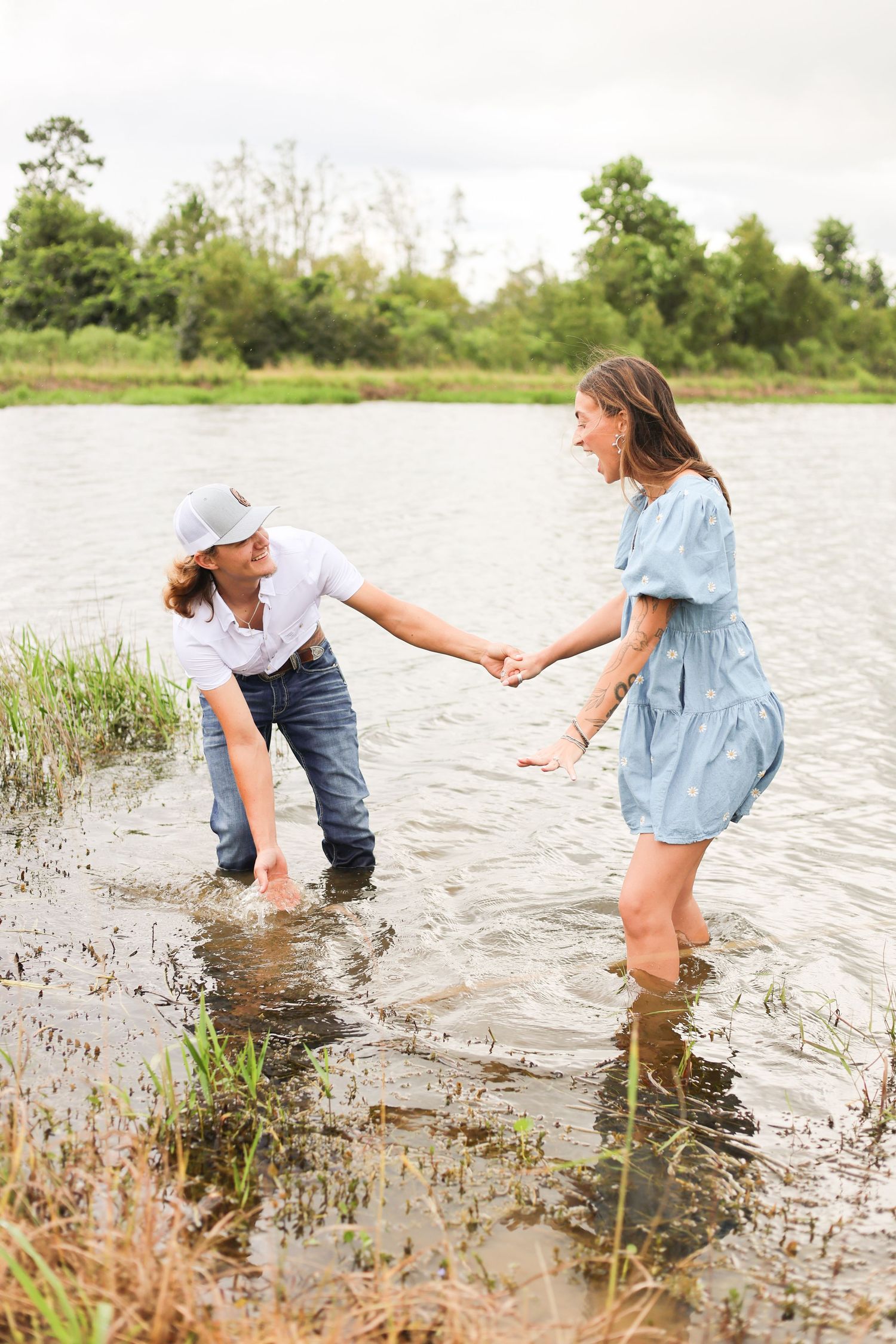 Couple splashing and playing in shallow water surrounded by marsh grass.