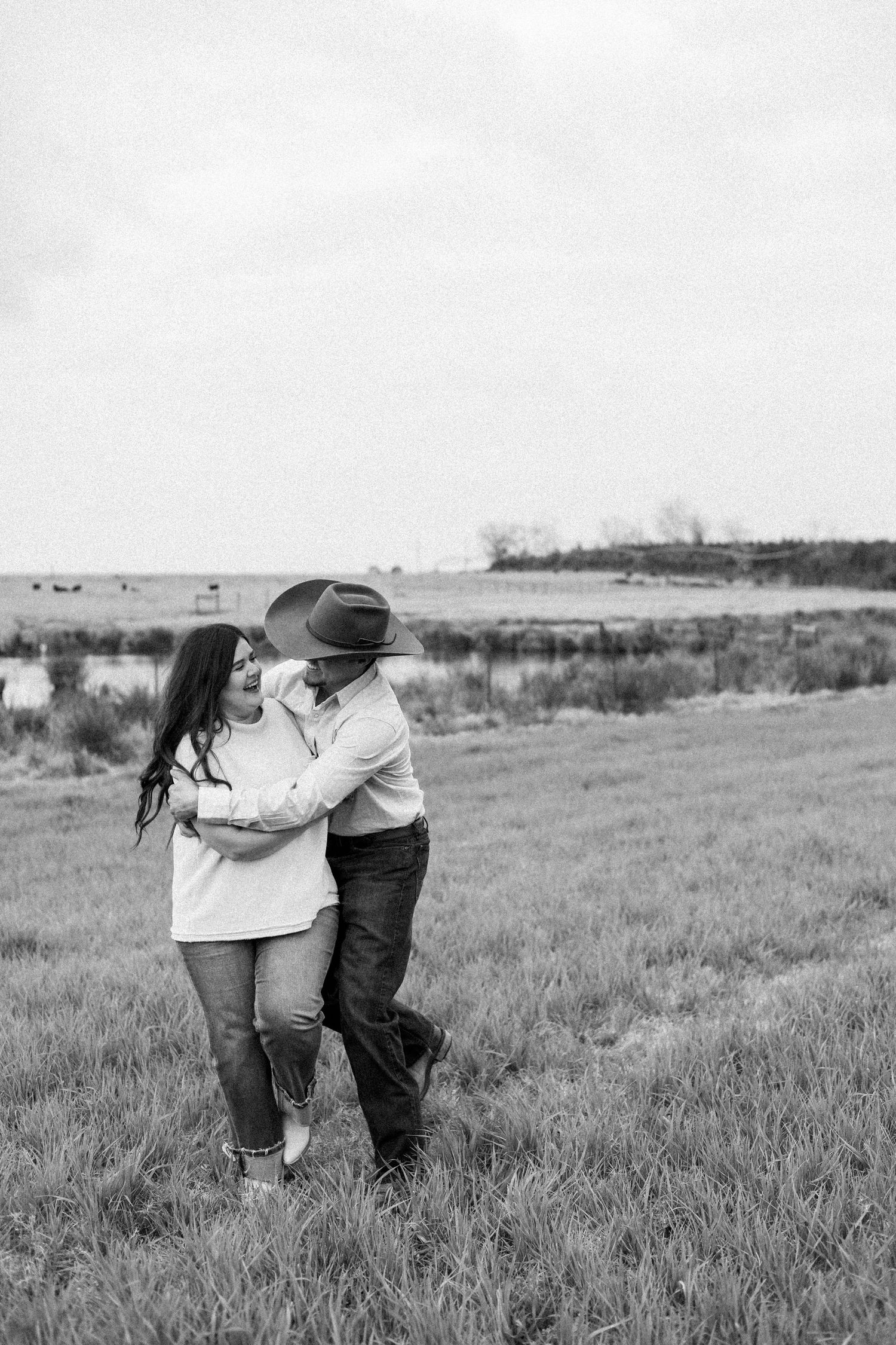 A couple embracing in a rustic field with rolling hills in the background.