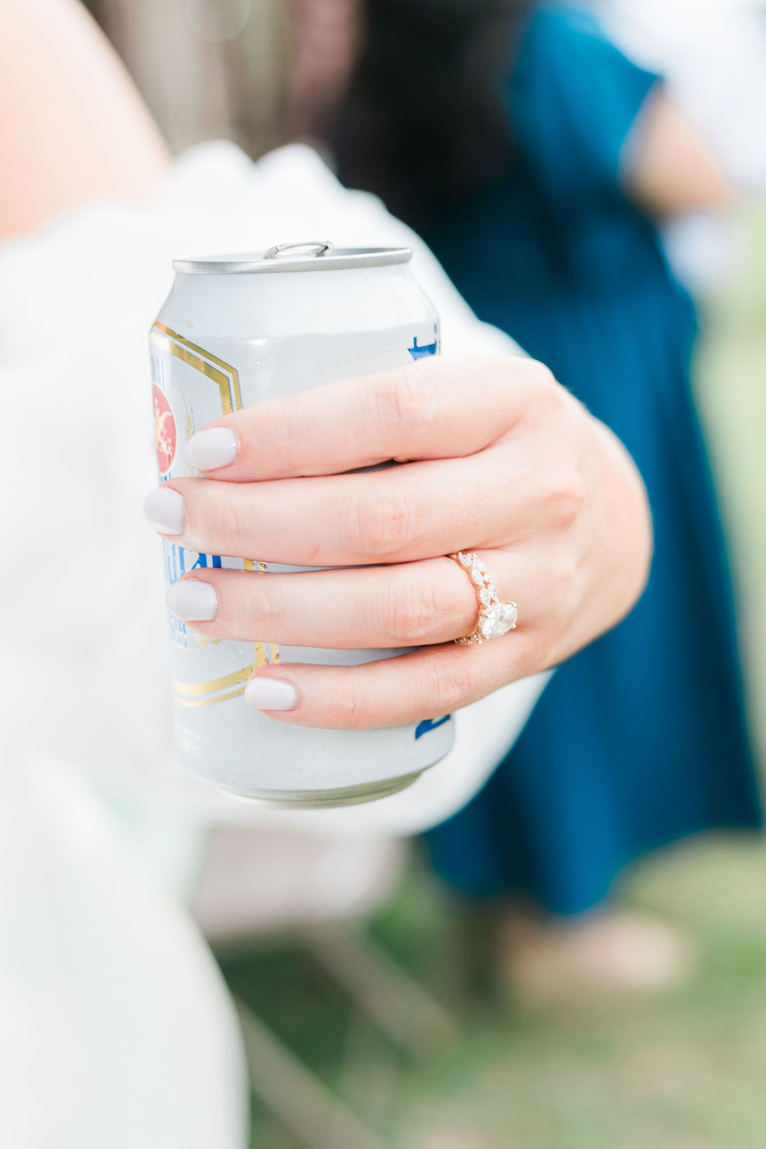 Bride with manicured nails and diamond ring holding silver beverage can at wedding reception.
