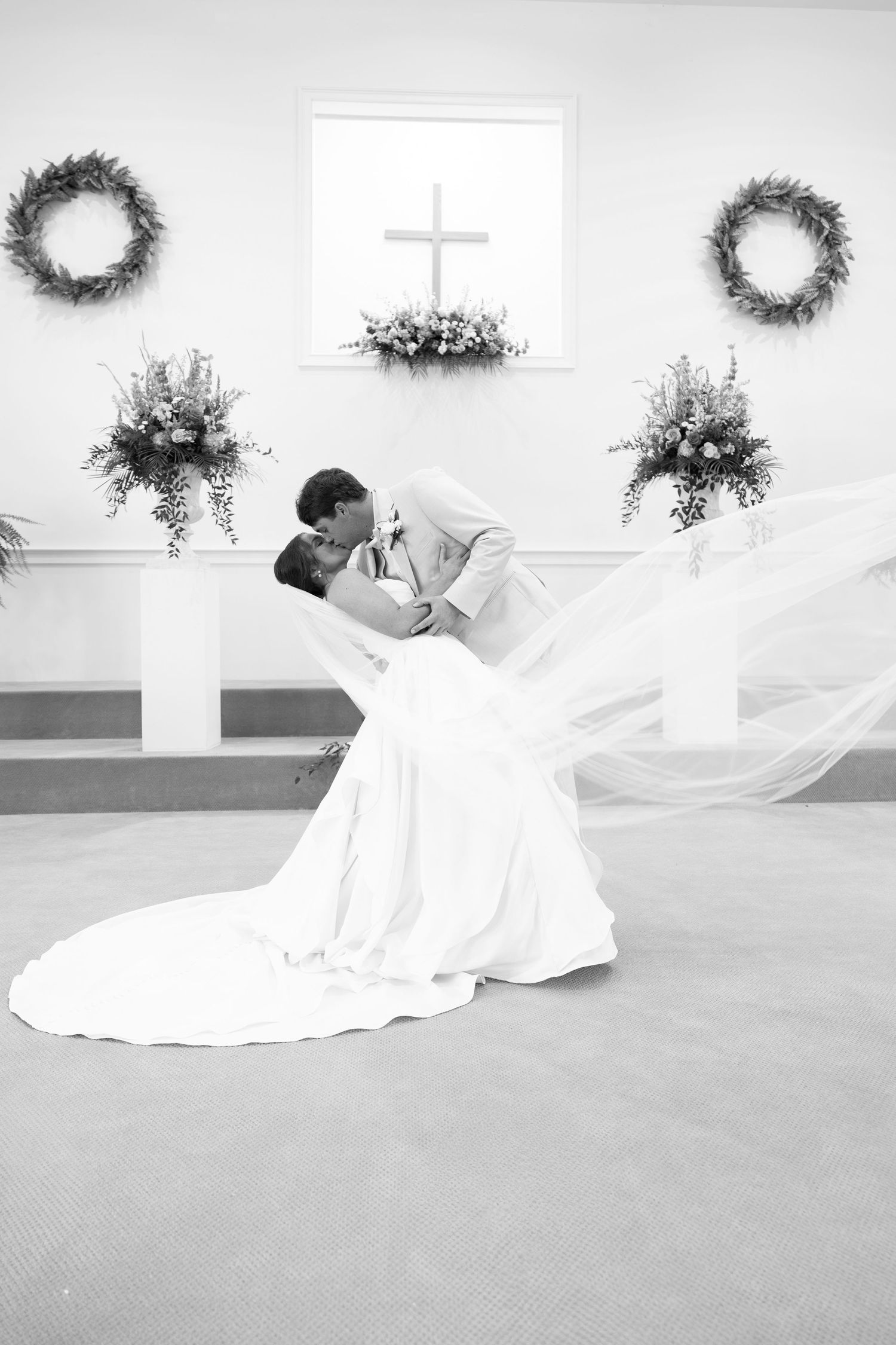 Bride and groom share a romantic dip kiss at the altar of a white church during their wedding ceremony.