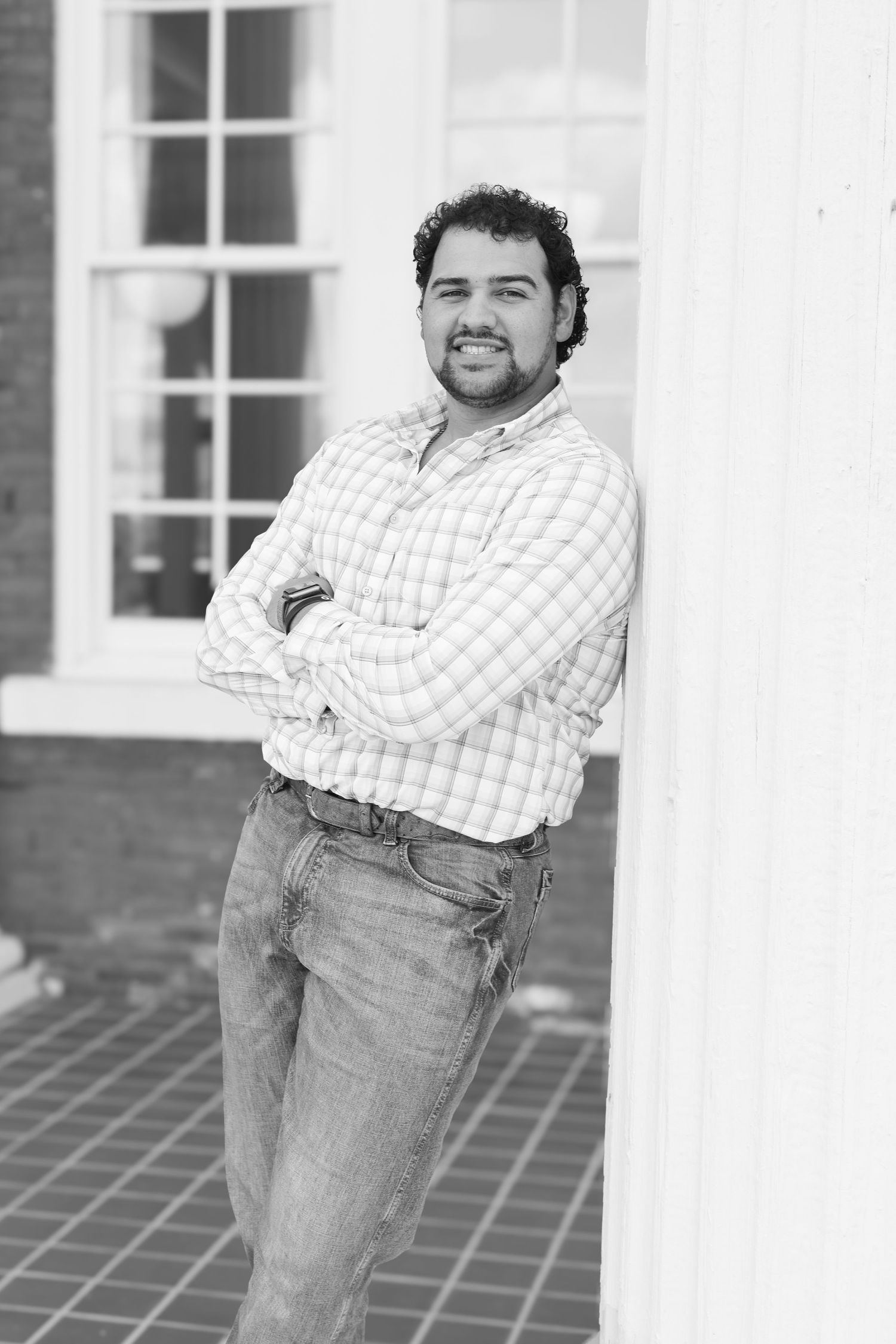 Person in plaid shirt leans against white column for casual portrait.