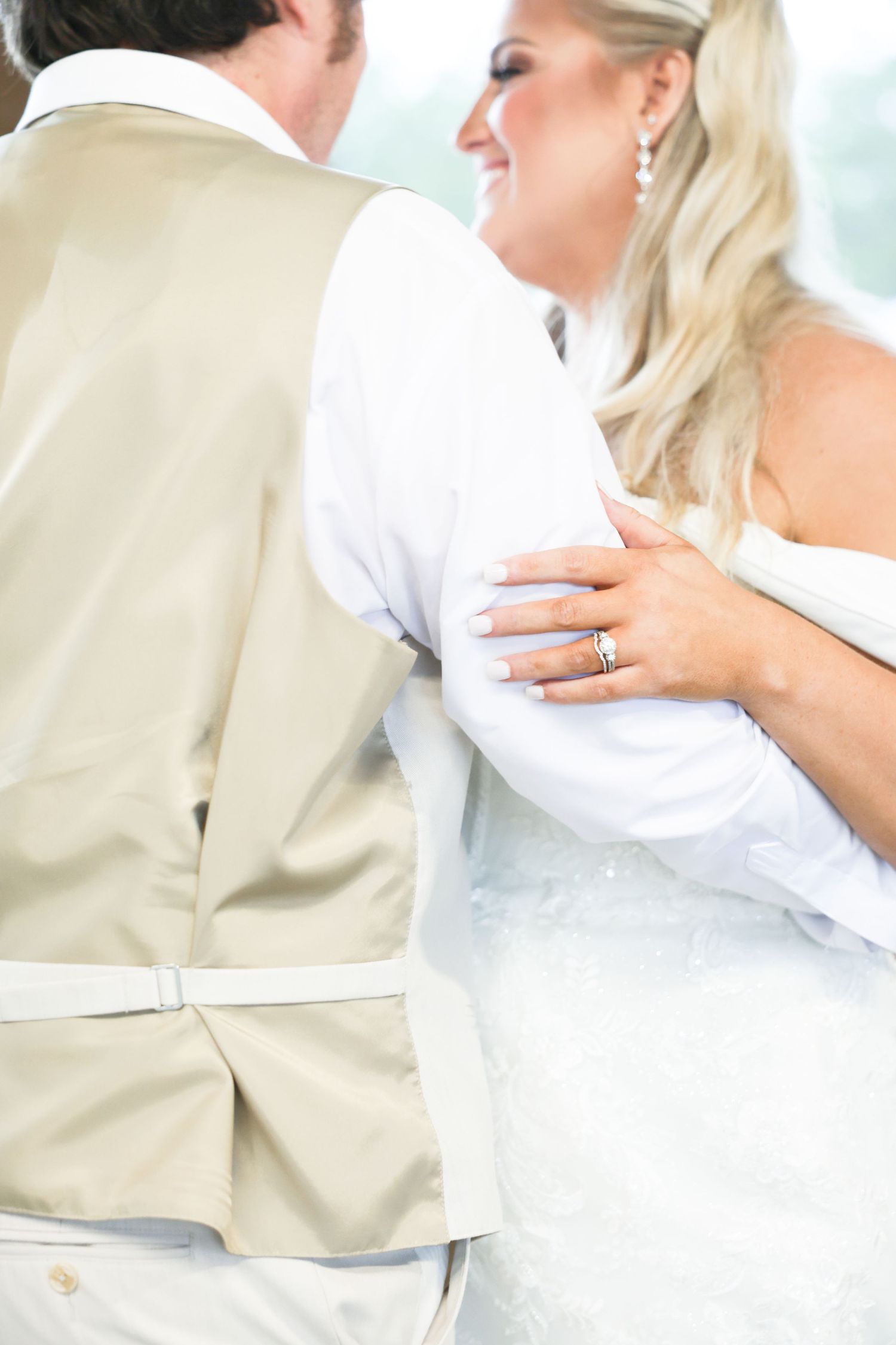 A bride with wedding ring embraces her groom in a tan suit during their first dance.