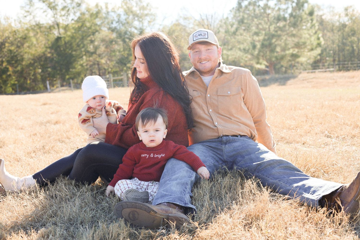 A family relaxes together on a grassy hillside during a sunny autumn afternoon in casual attire.