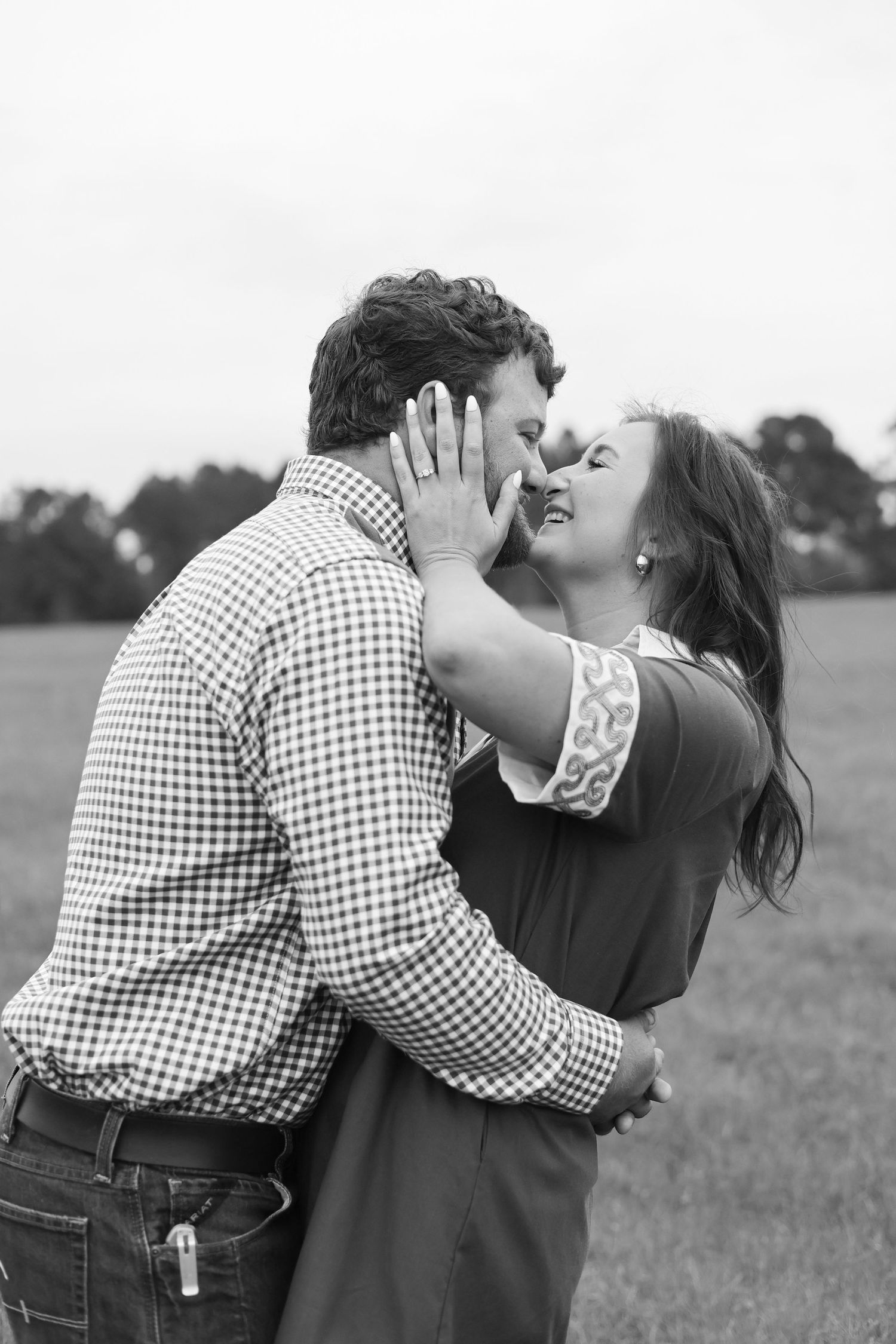 A black and white photo capturing an intimate romantic moment between a couple in a field.
