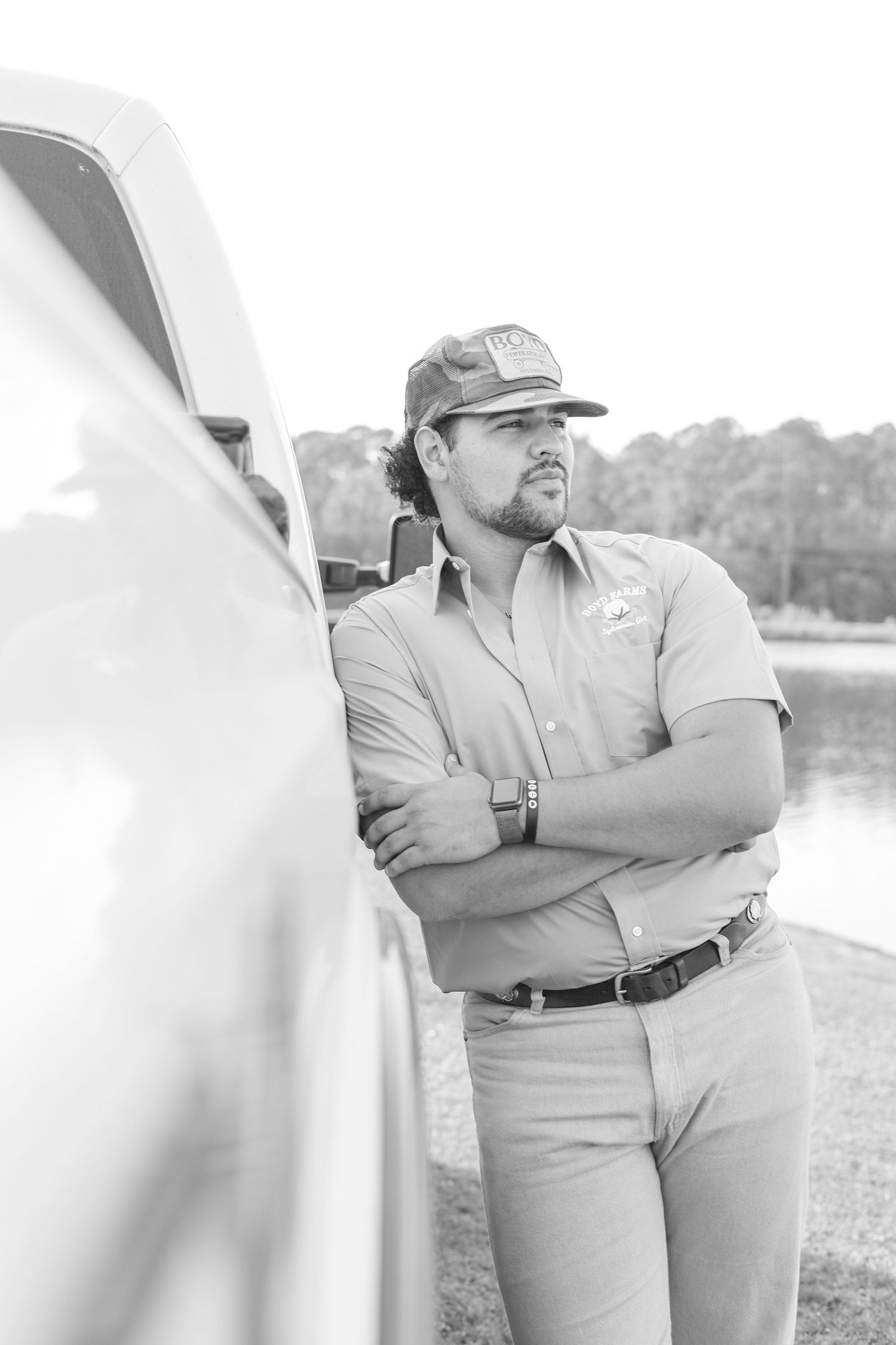 Black and white photo of person in uniform looking away while leaning on truck.