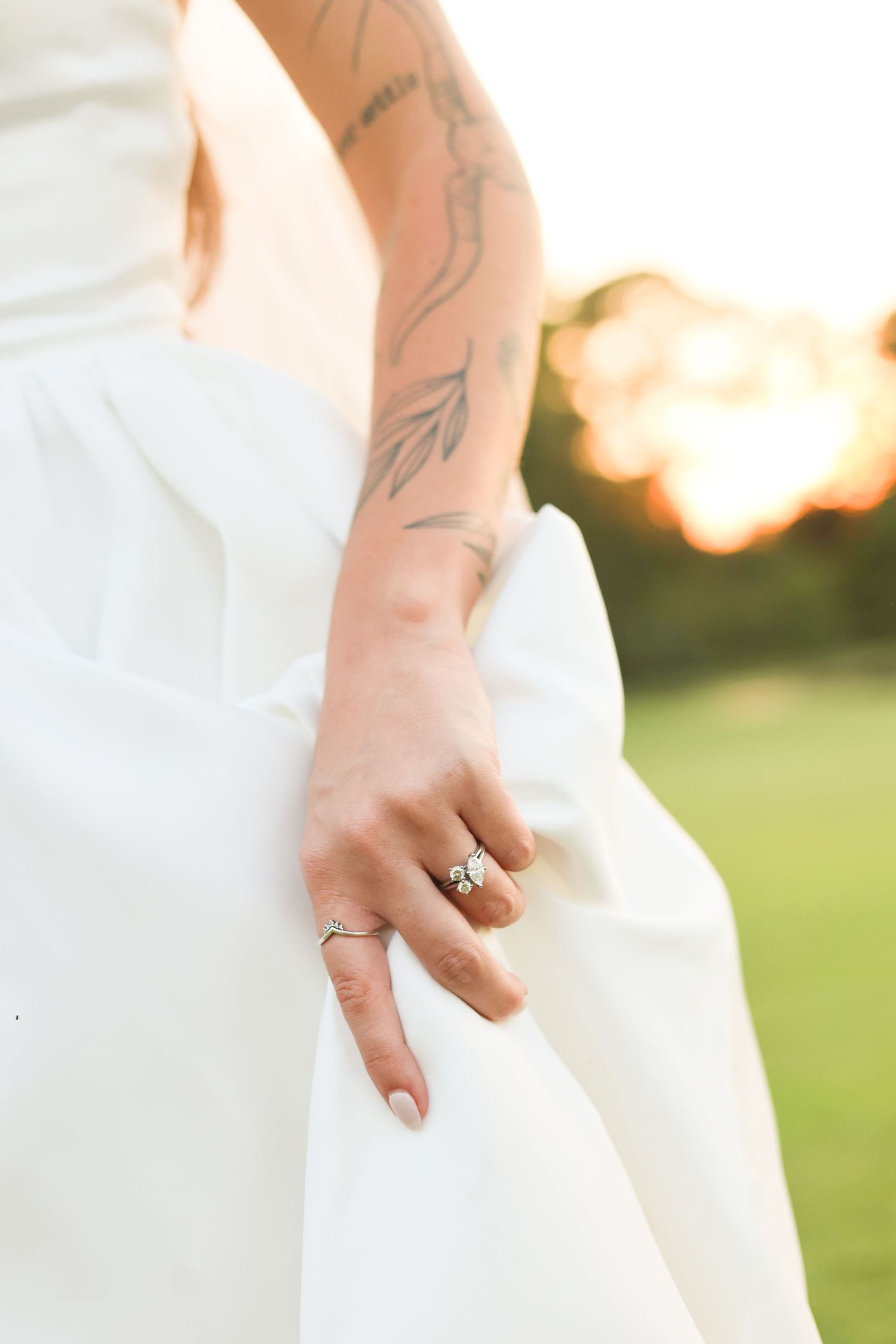 Close-up of hands in a white wedding dress showing engagement ring and tattoos.