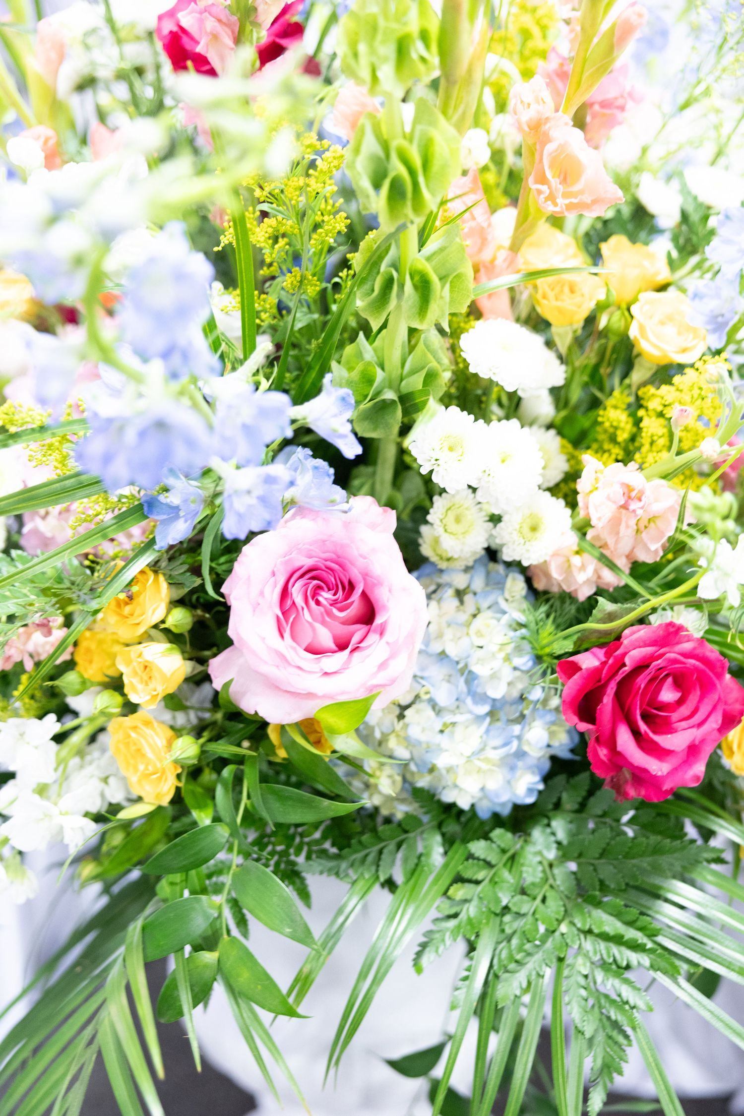 Colorful floral arrangement featuring pink roses, blue hydrangeas, yellow blooms, and lush green foliage in a vibrant bouquet.