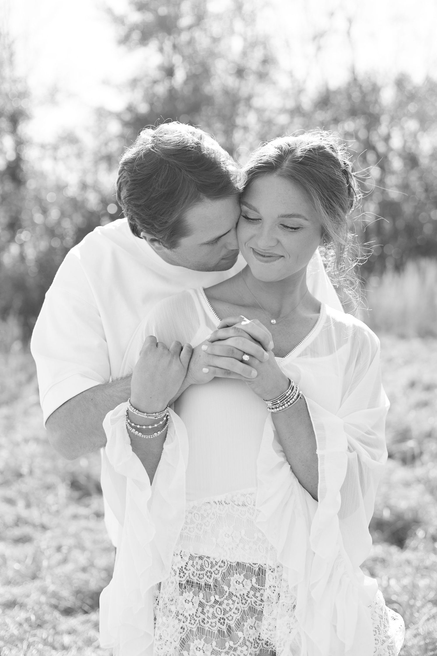 Romantic black and white portrait of a couple embracing outdoors with soft natural backlighting.