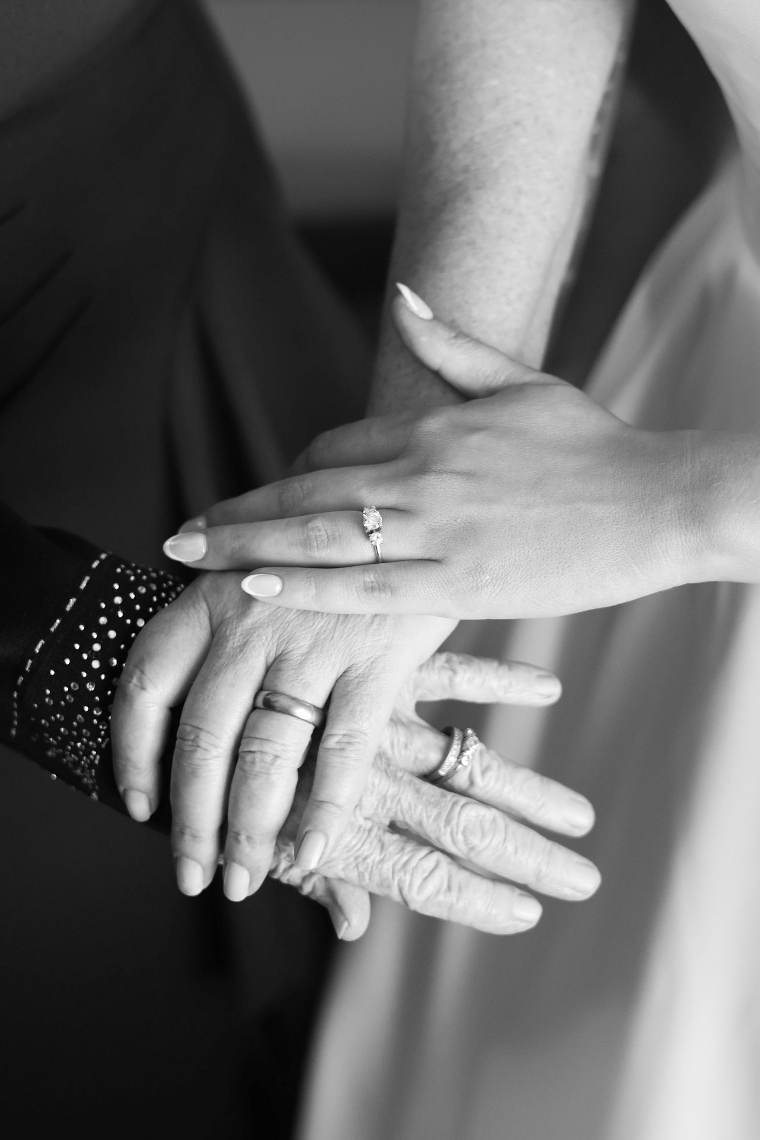 Black and white close-up of hands with wedding rings stacked together showing three generations.