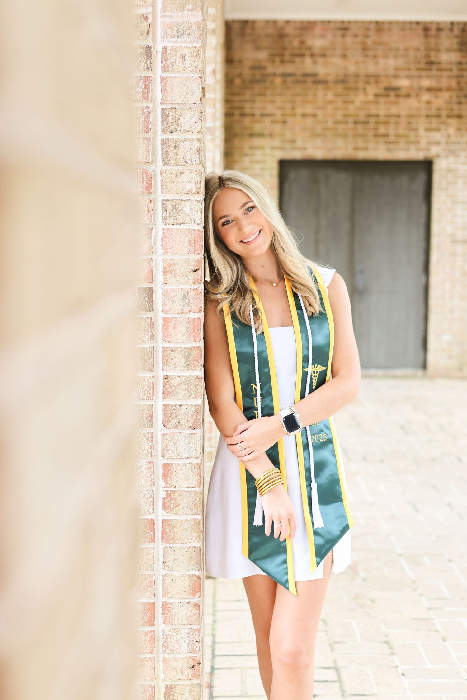 Graduate in green graduation stole stands near brick columns.