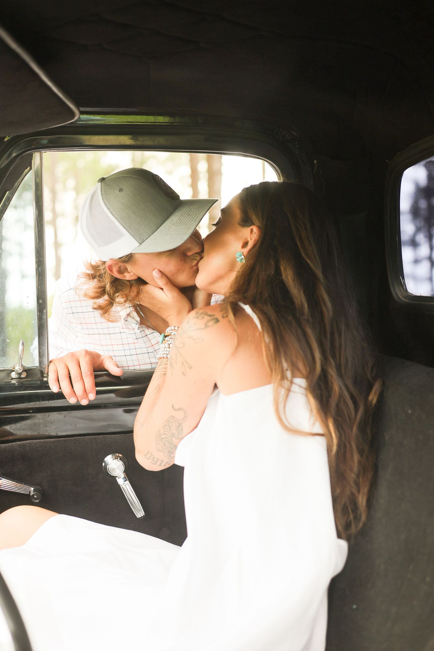Inside a vintage car, a couple shares a romantic embrace in natural lighting.