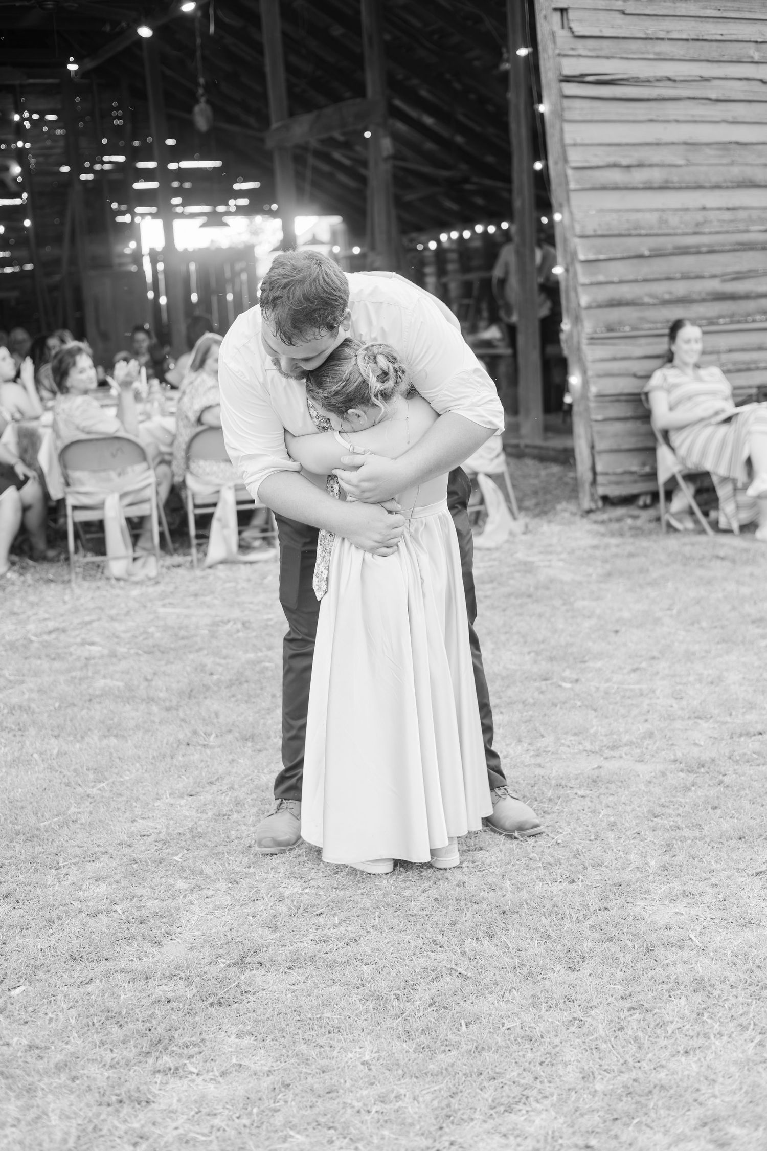 Black and white photo of bride and groom sharing an emotional embrace during first dance at rustic barn wedding reception.