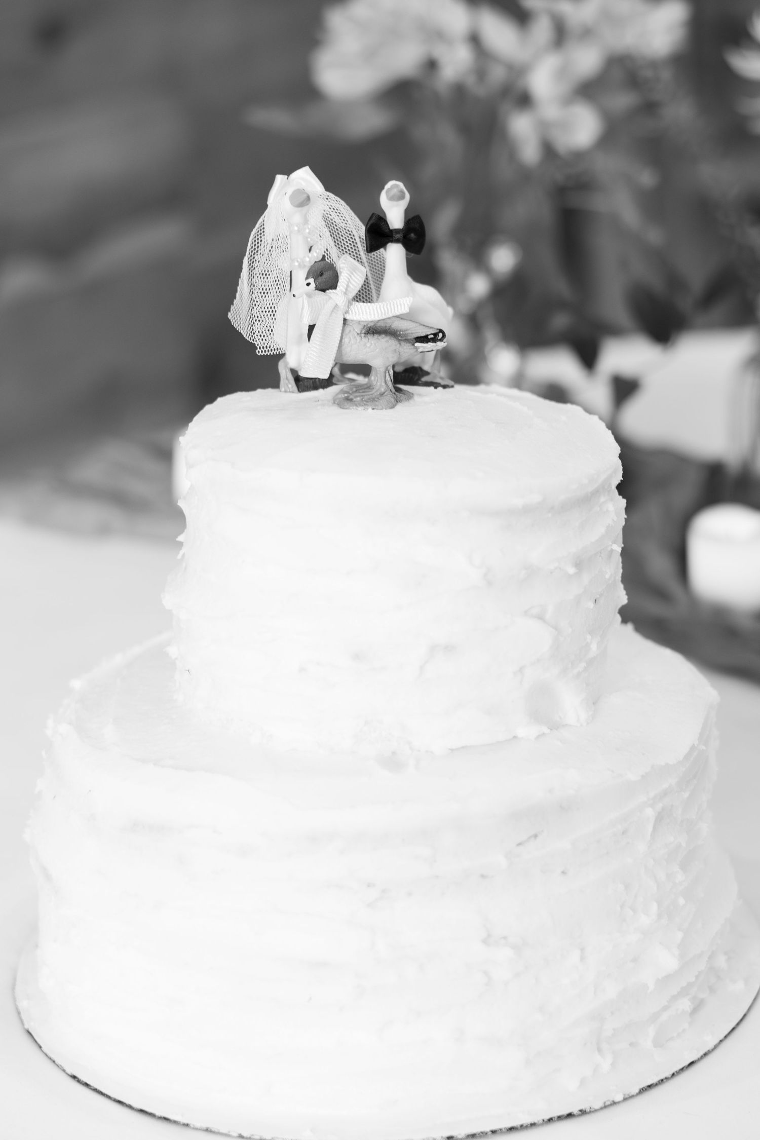Black and white photo of a two-tier white wedding cake topped with bride and groom figurines.