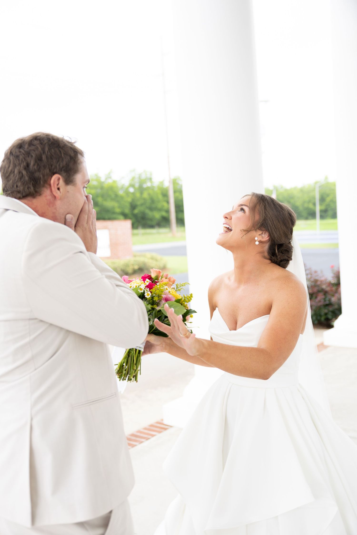 Bride in white strapless gown laughing with emotional groom during wedding first look ceremony.
