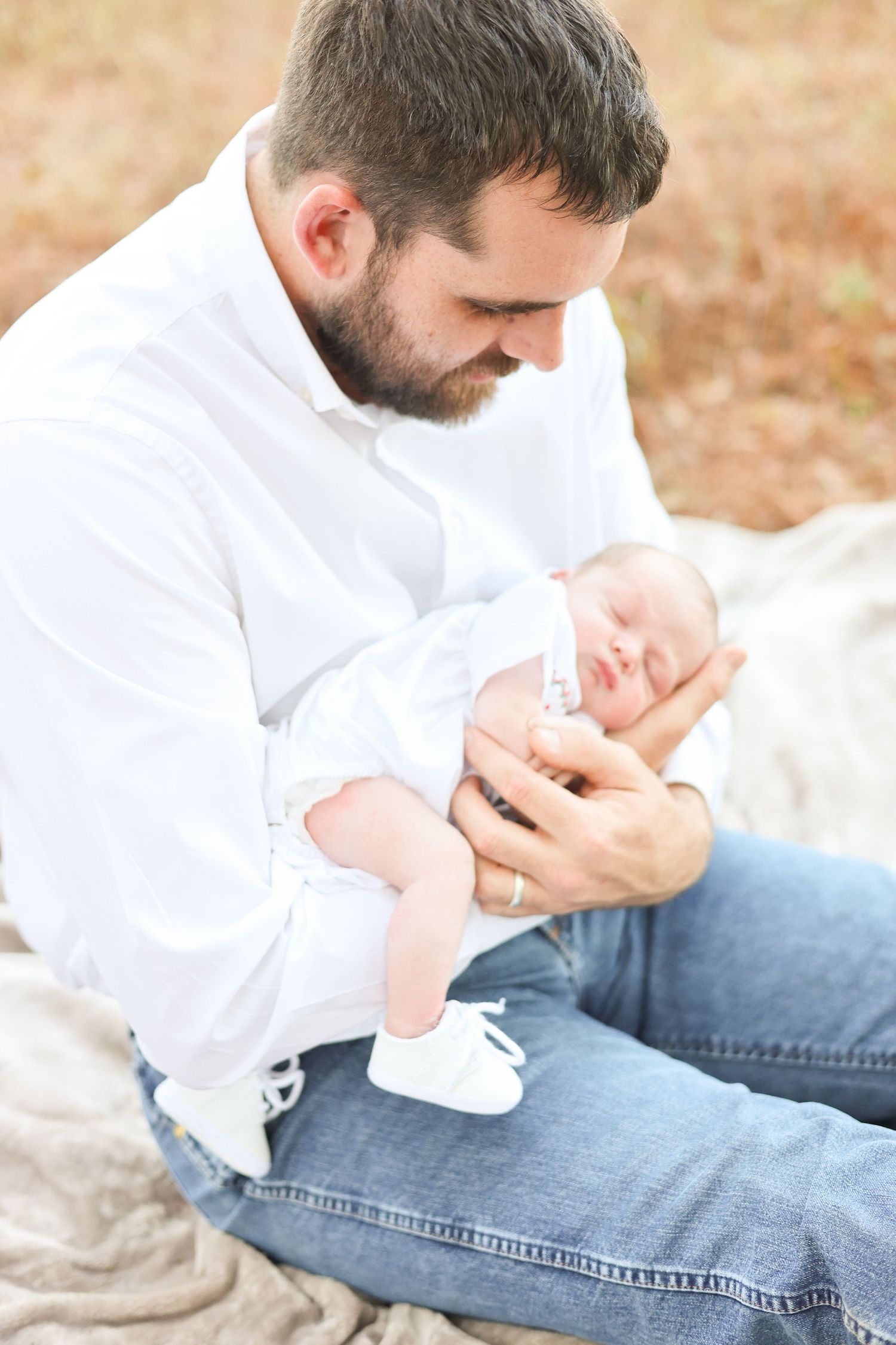 A tender moment between parent and infant outdoors on a blanket, wearing a white shirt and jeans.