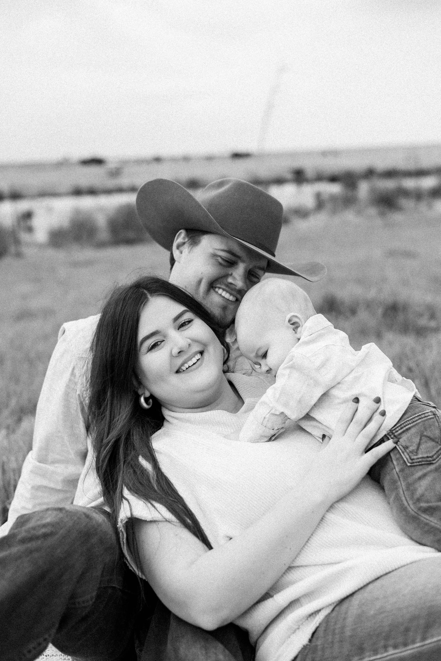 A family cuddling together on a blanket in a serene countryside setting.