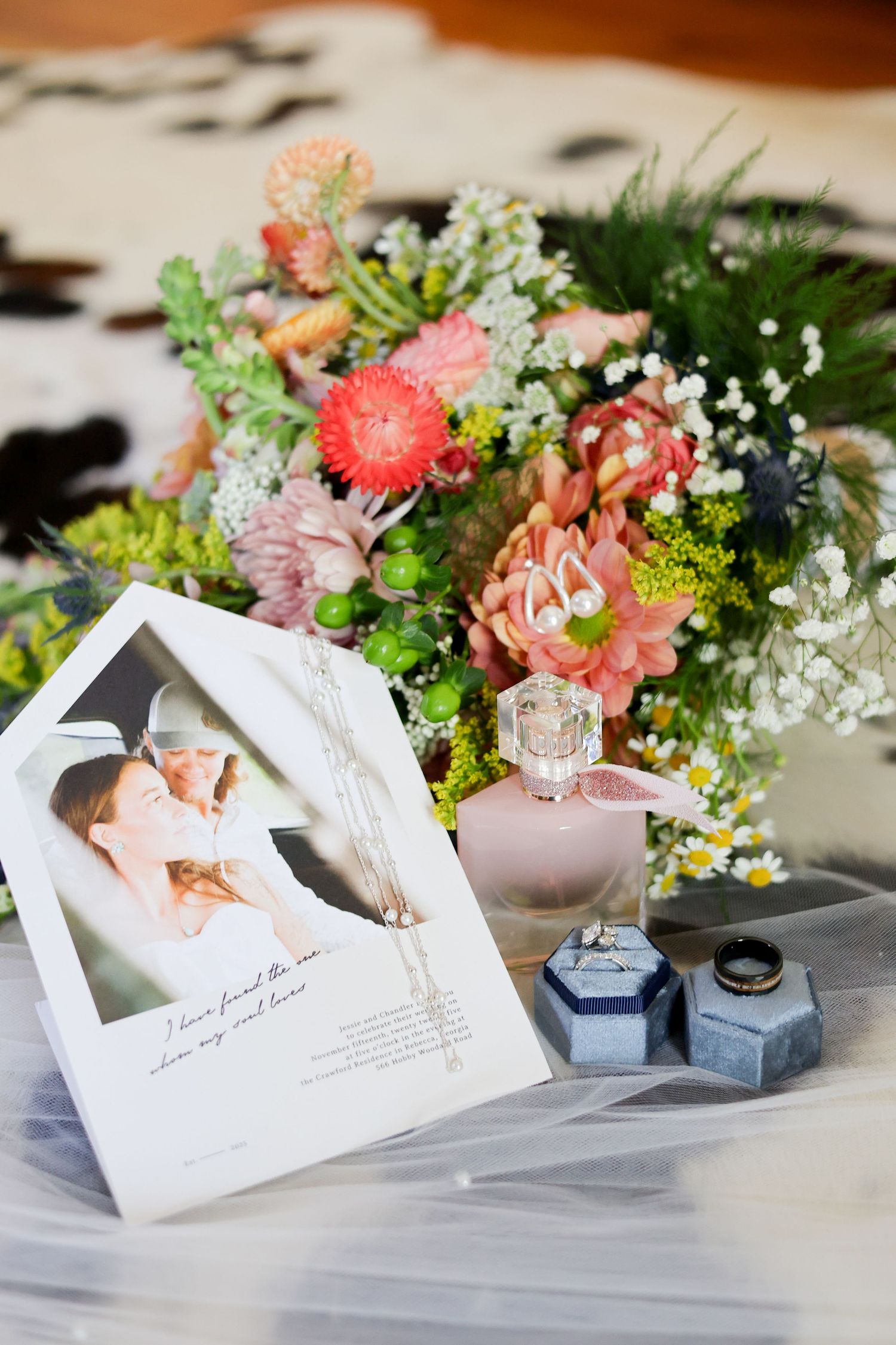 Colorful floral arrangement with pink and white flowers next to wedding photos and ring boxes.
