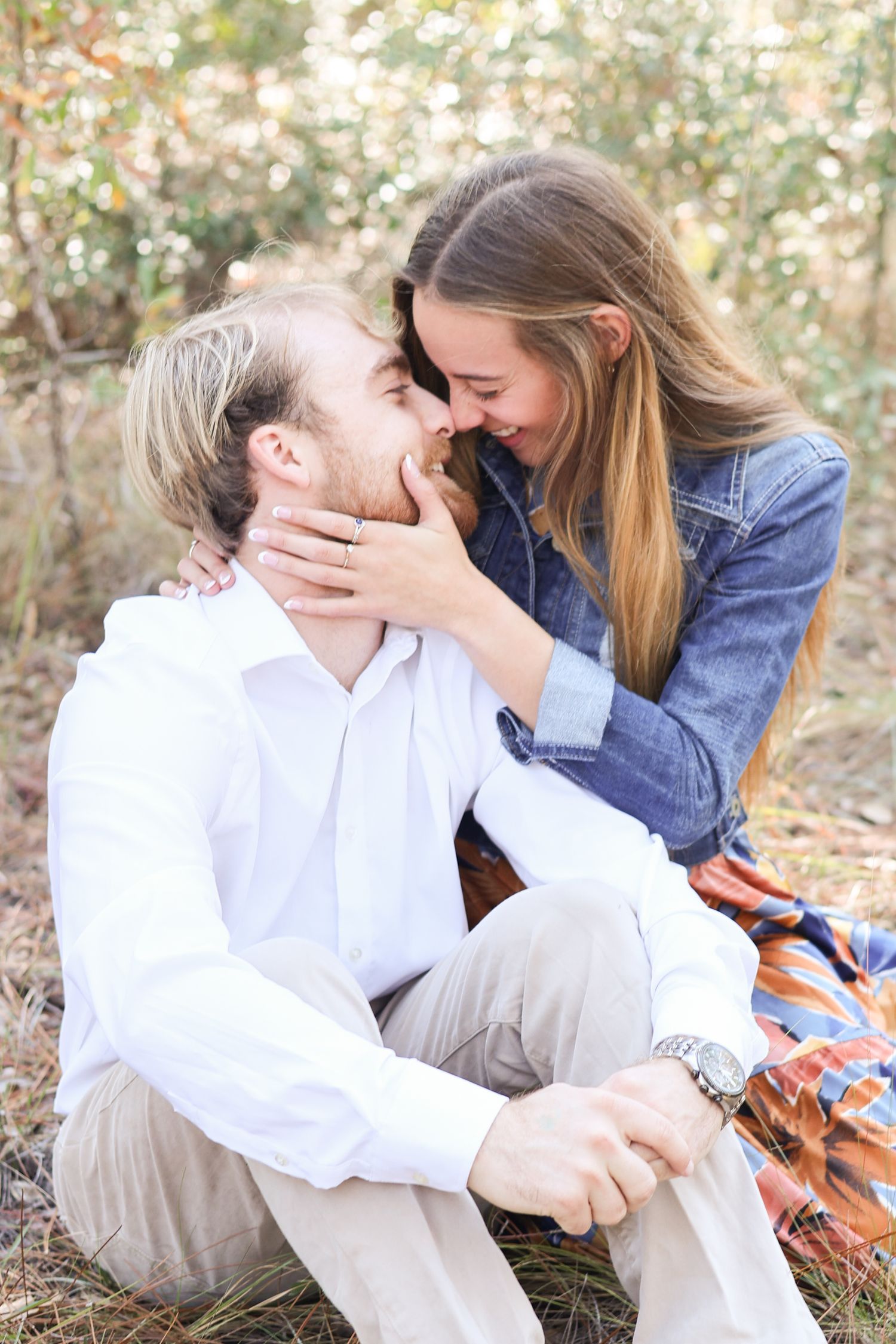 A romantic outdoor engagement photo of a couple sharing a tender moment on a picnic blanket.