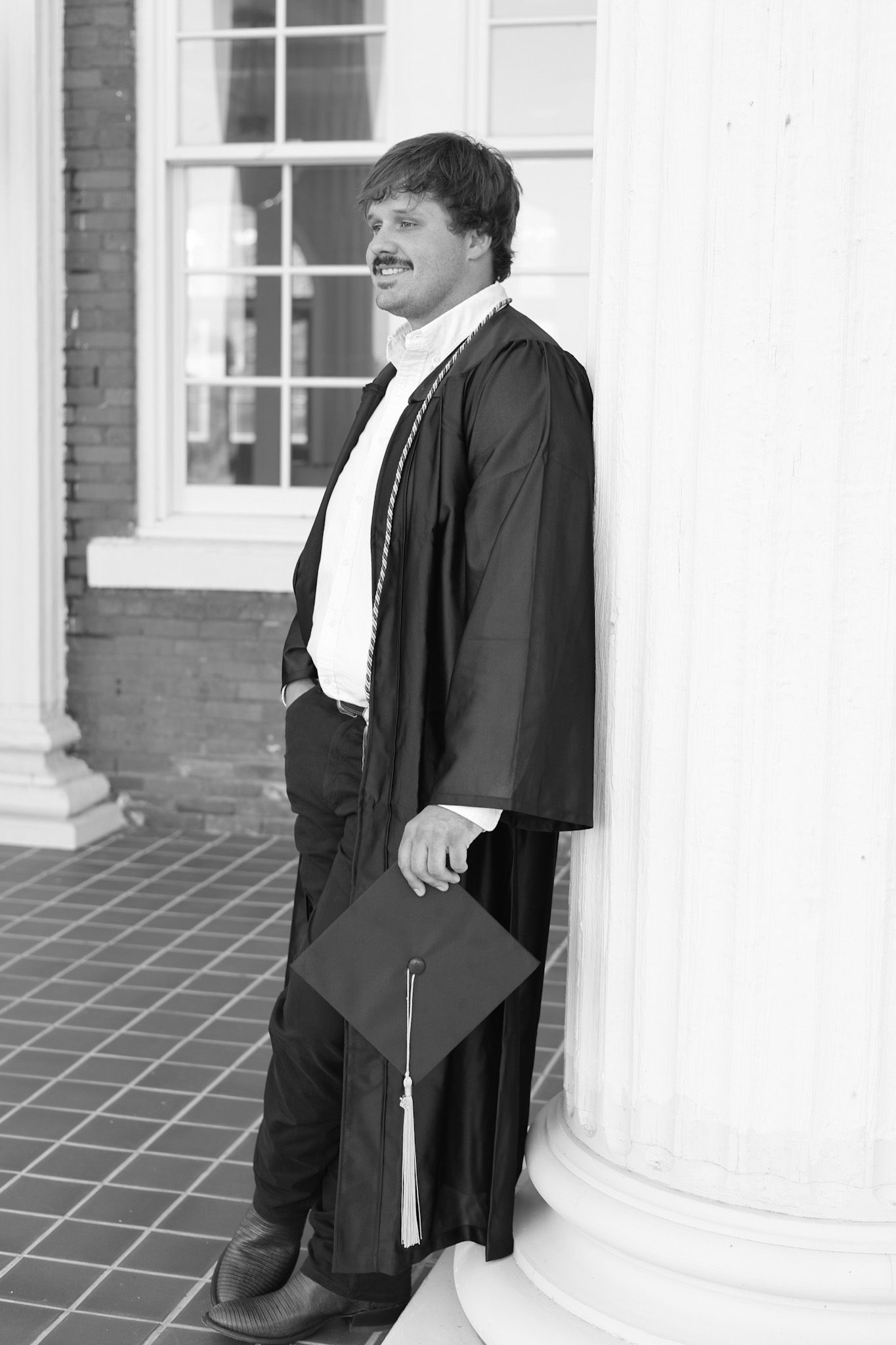 Graduate in academic regalia standing between white columns in formal portrait.