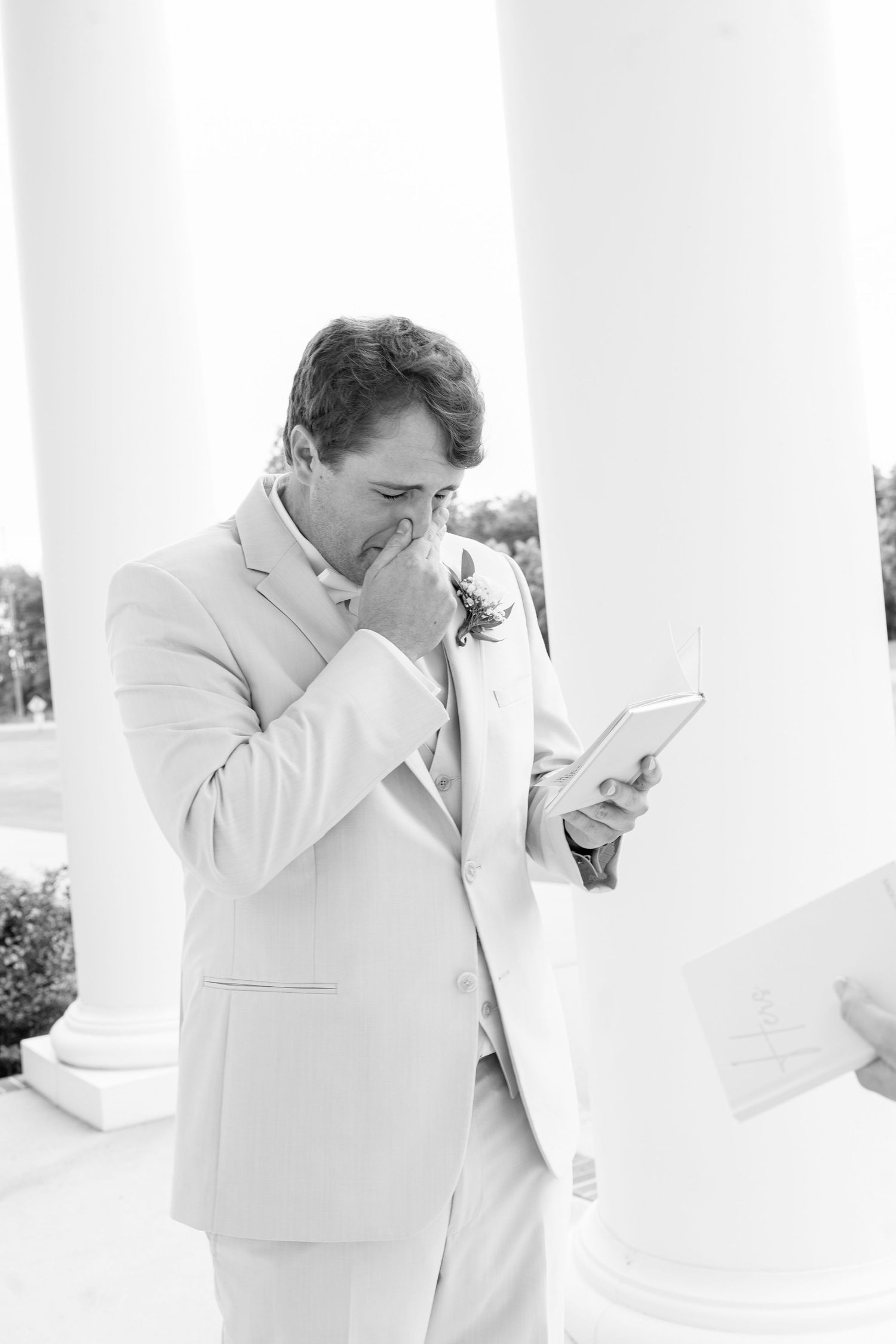 Tearful groom in beige suit reading heartfelt letter before wedding ceremony.