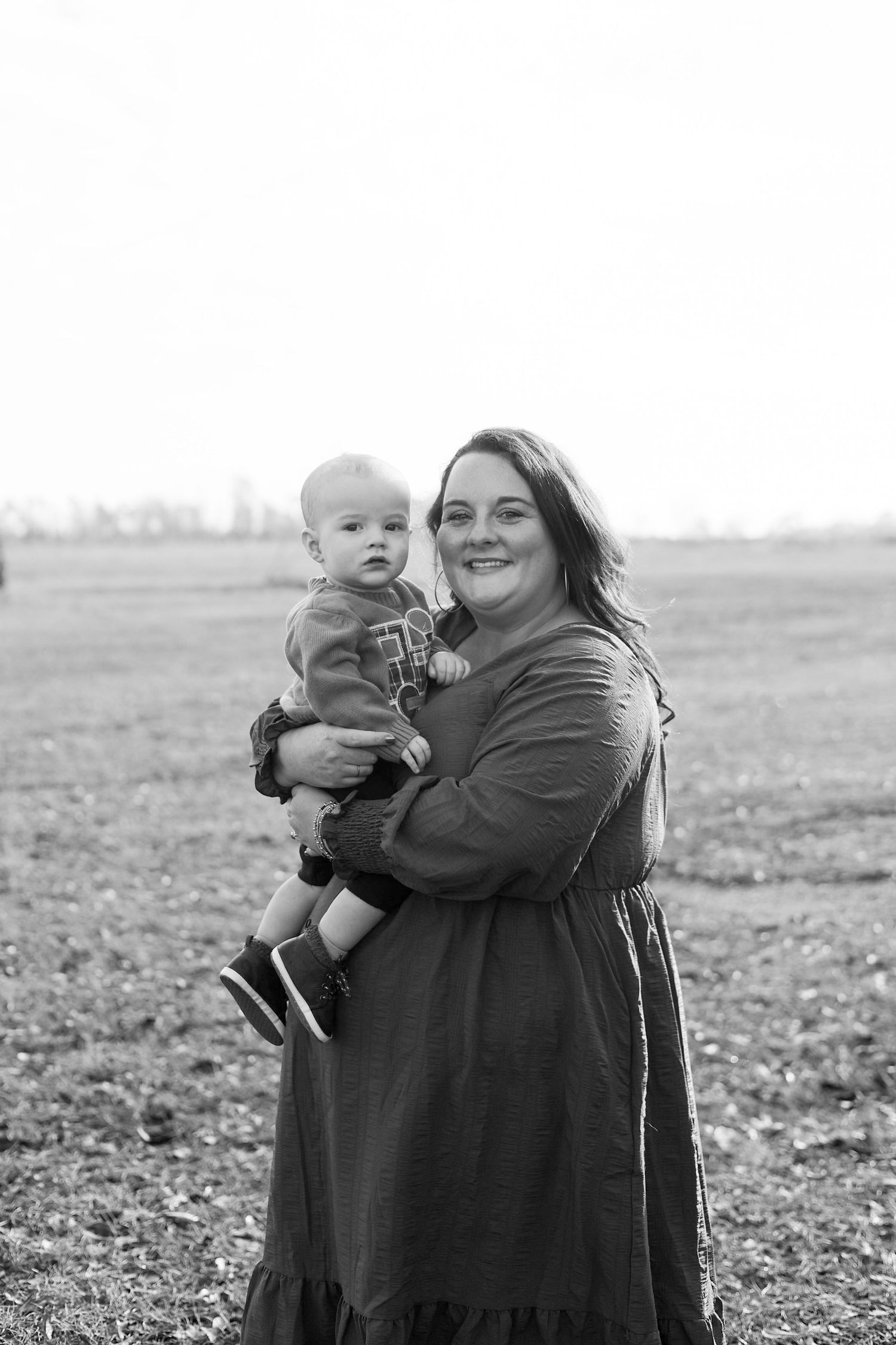 A parent and baby share tender moments in a series of black and white photos taken in an open field.
