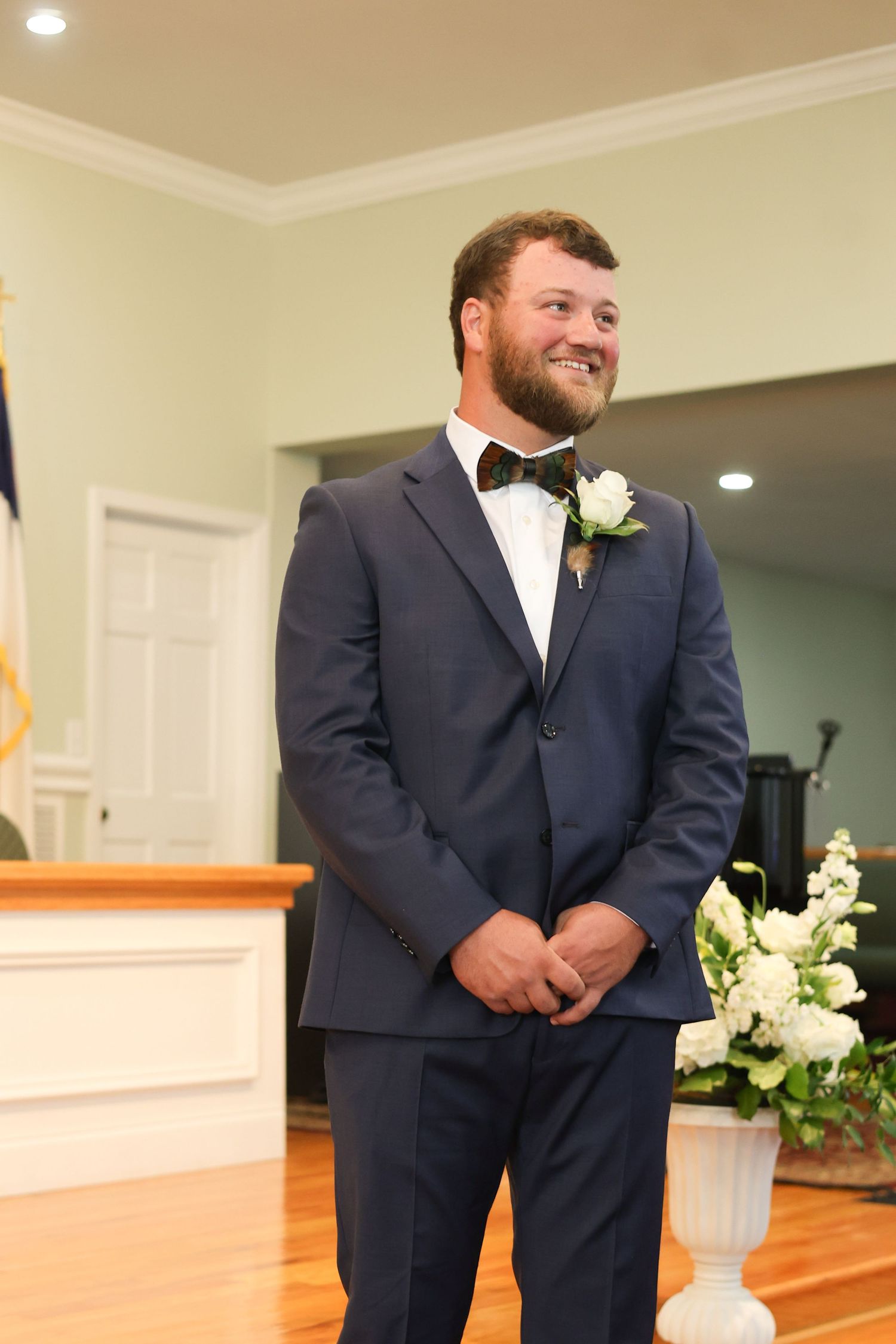 A groomsman in a navy suit stands at the altar during a wedding ceremony.