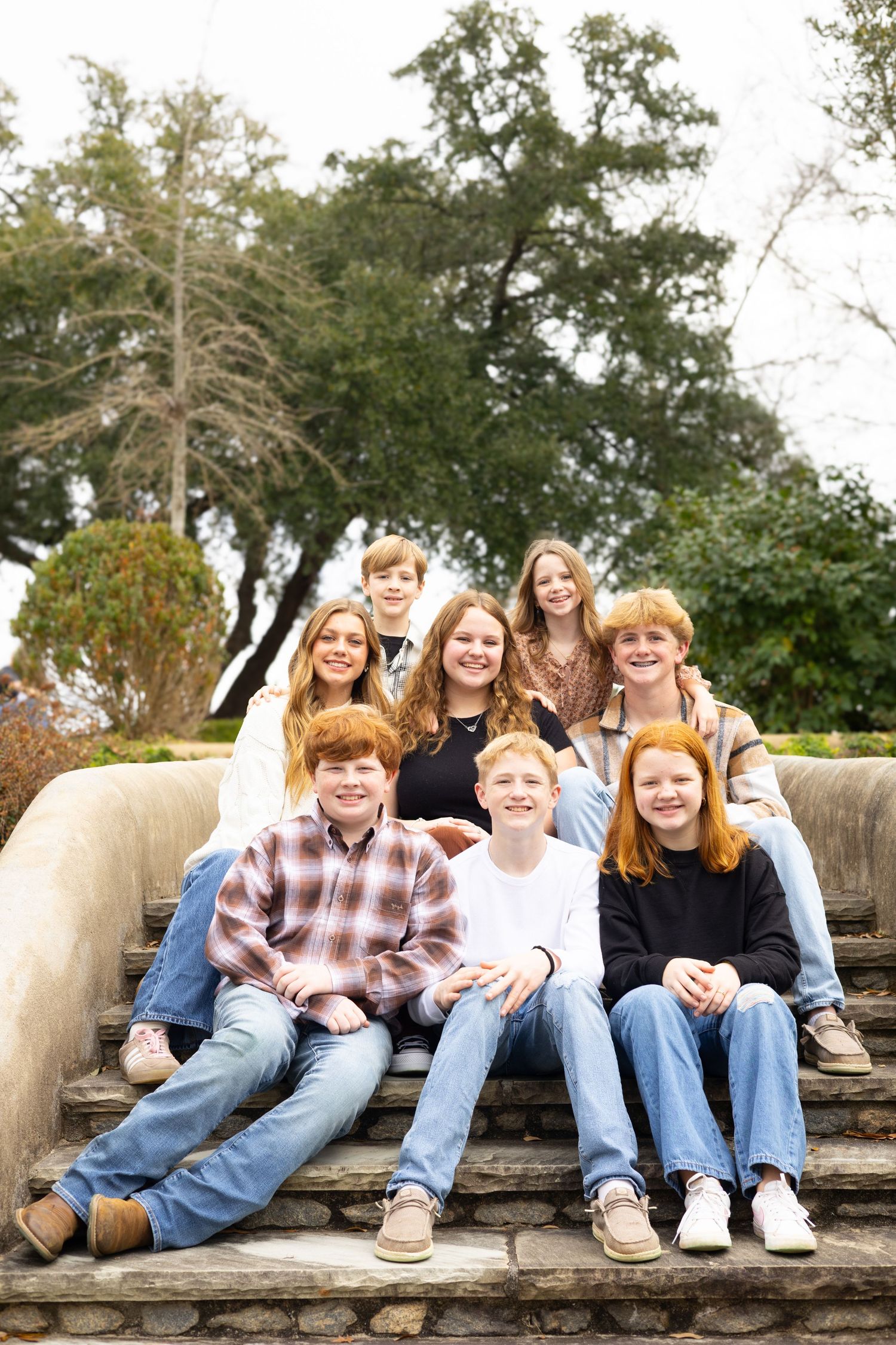 A group sits together on outdoor stone steps surrounded by trees and greenery on a sunny day.