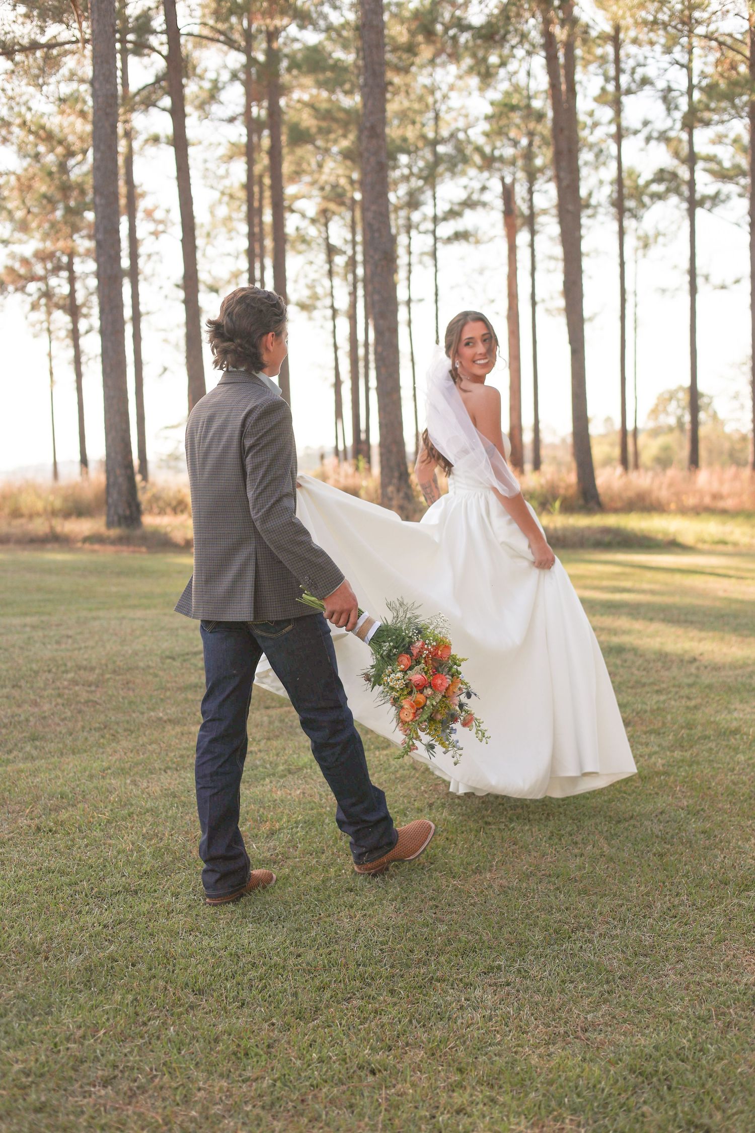 A playful wedding moment captured in a sunlit forest clearing with flowing white dress.