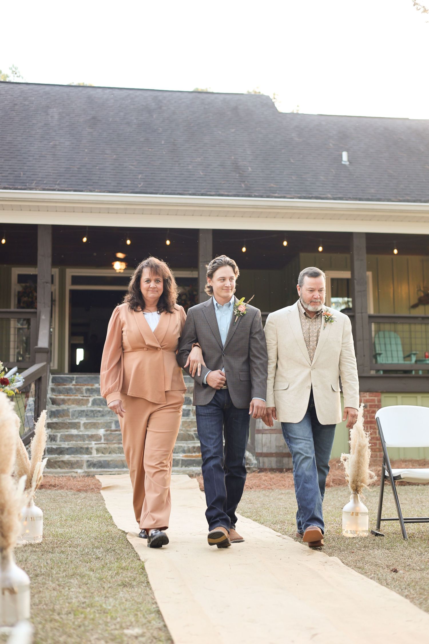 Wedding guests in formal attire walk down an outdoor pathway at dusk.