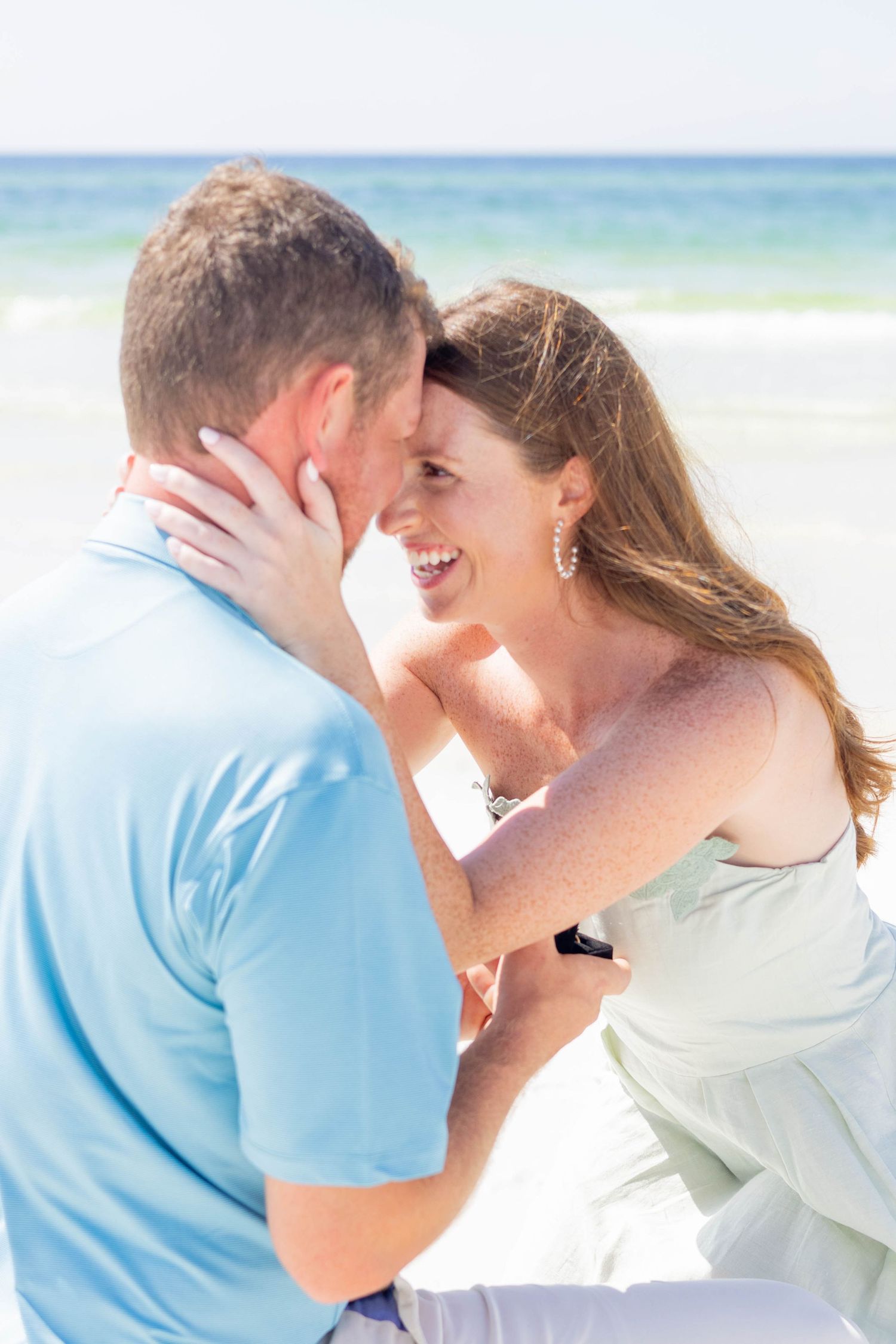 Newly engaged couple embracing and smiling face to face on a bright sunny beach.