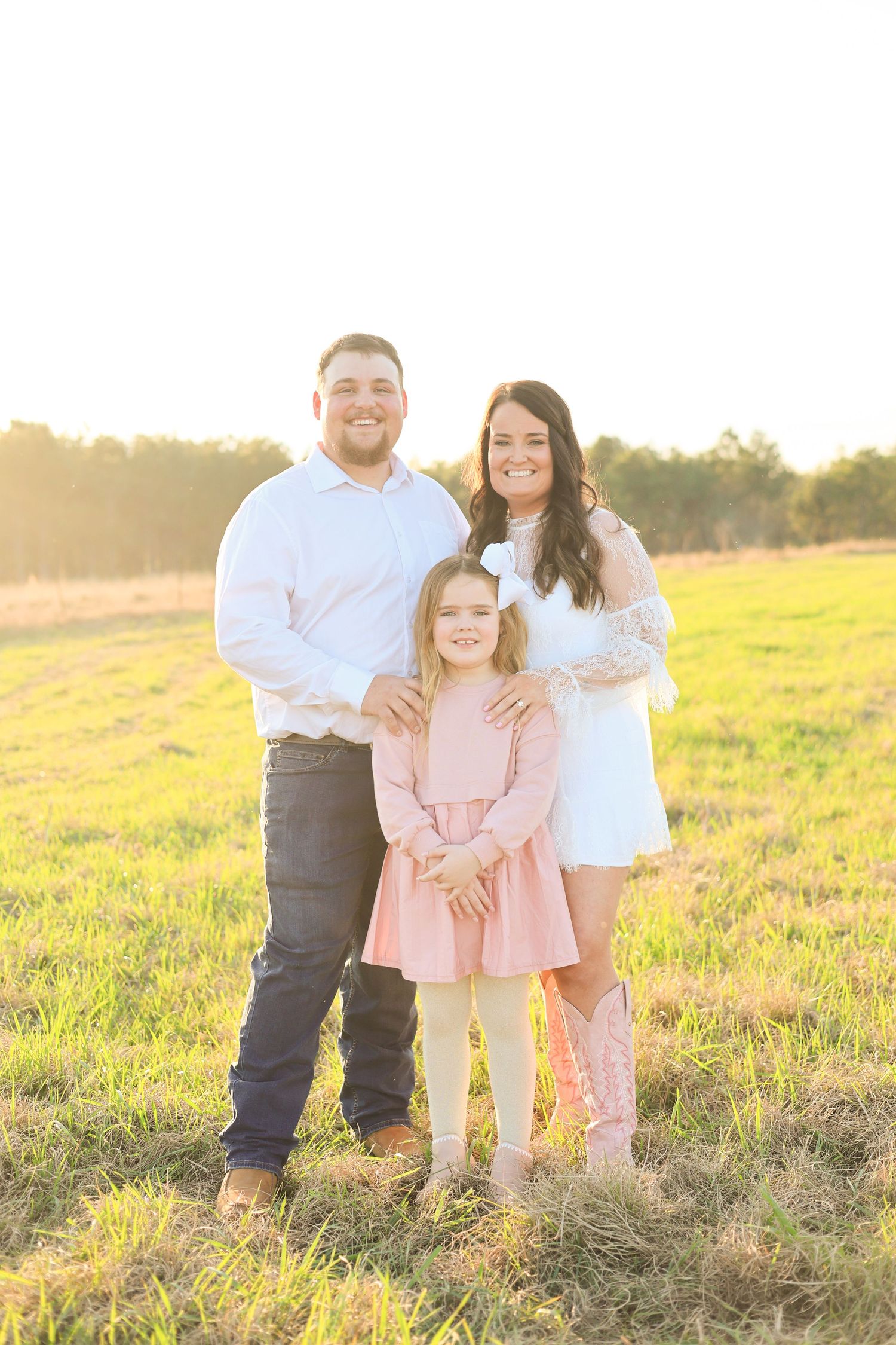 Family wearing coordinated outfits poses together in a sunlit field during golden hour.