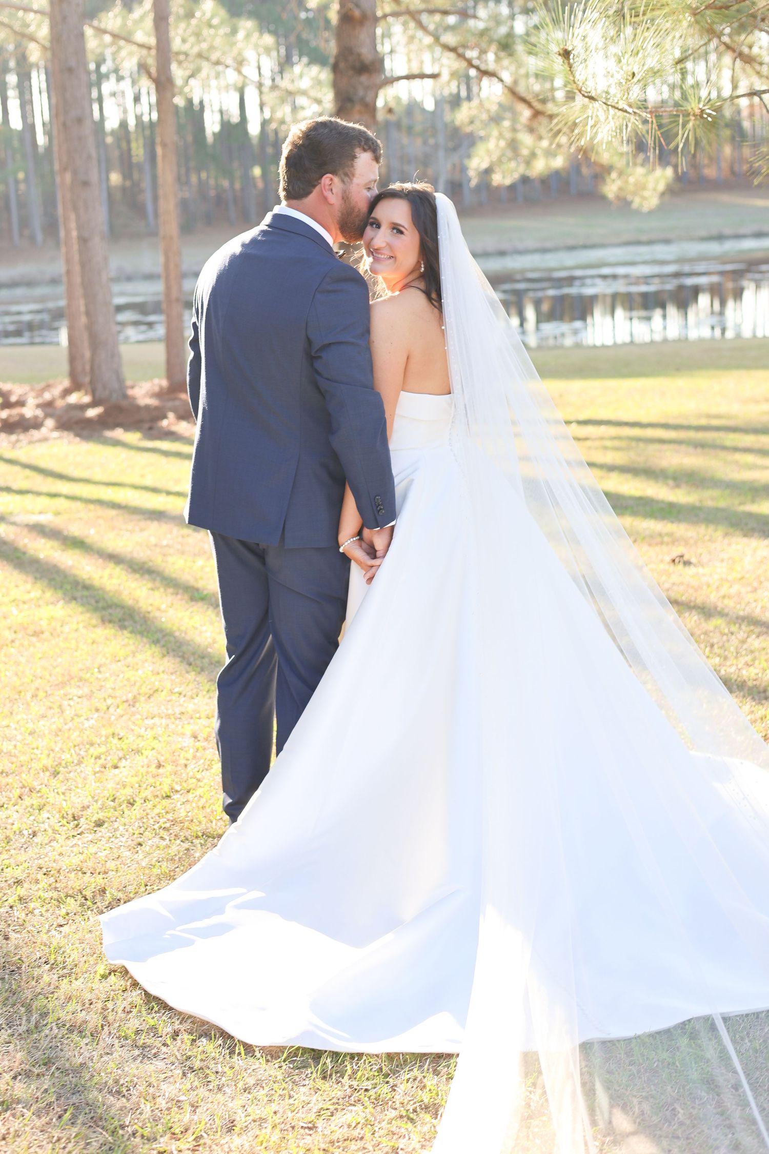 A couple in wedding attire dance together in a sunlit outdoor setting with fallen autumn leaves on the ground.