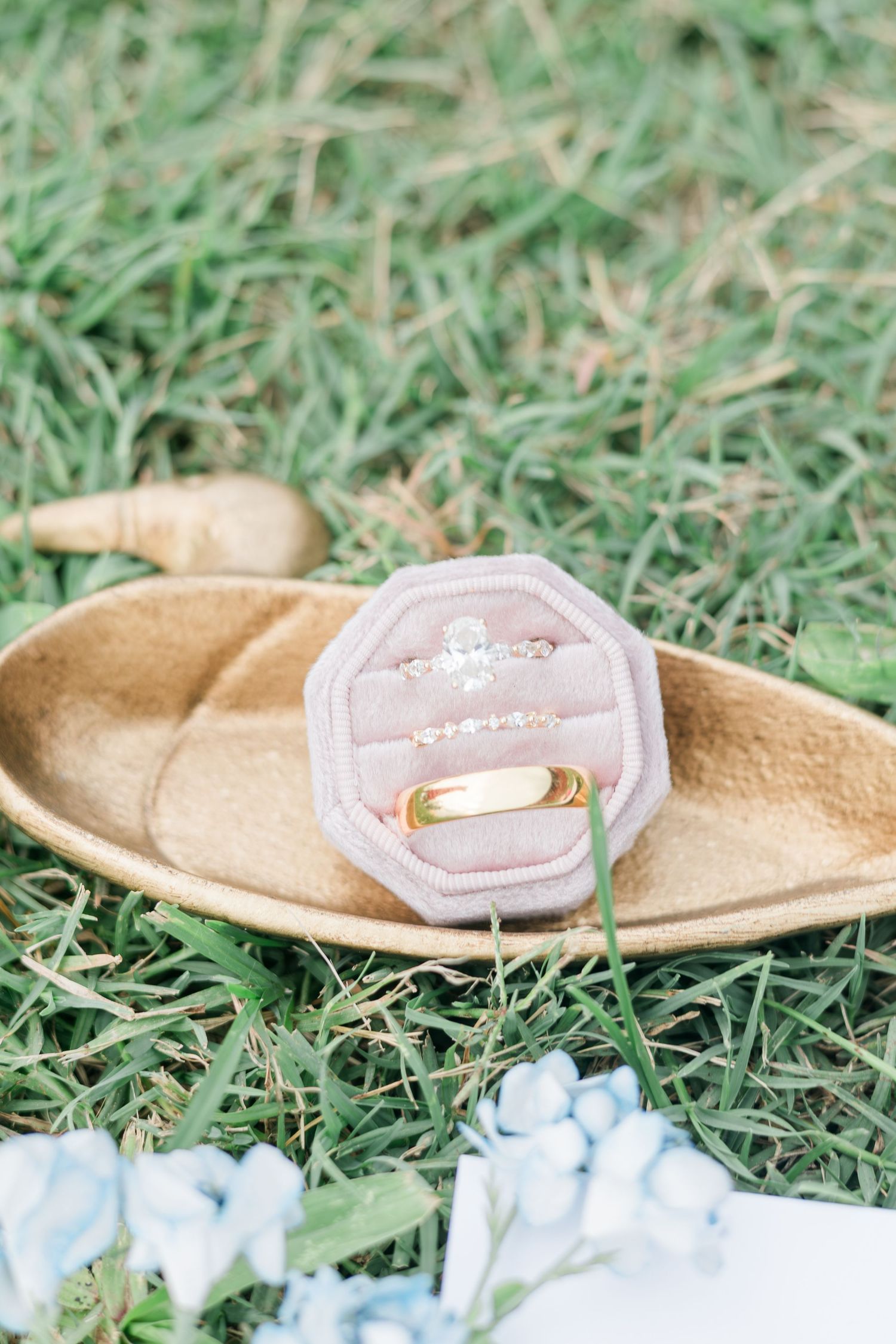 Diamond engagement ring and gold wedding band displayed in pink velvet ring box on grass.
