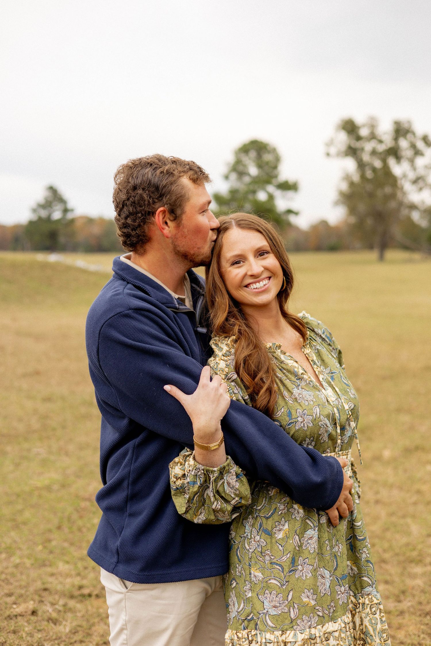 Romantic couple embracing in a sunny field wearing casual attire.