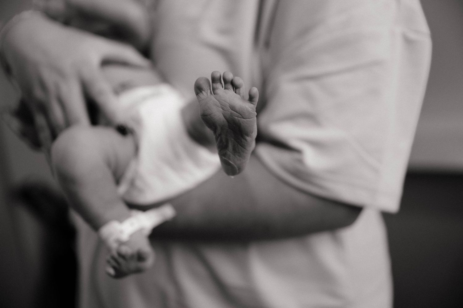 Black and white photo of an adult cradling a newborn baby, with tiny infant feet visible in the foreground.