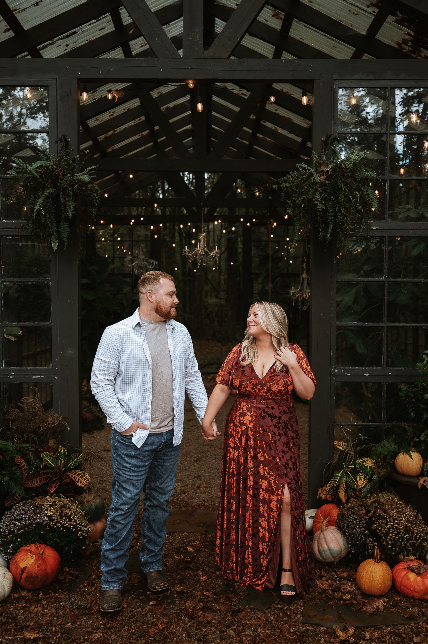 Couple sharing laughs in autumn greenhouse setting surrounded by pumpkins and fall decor.