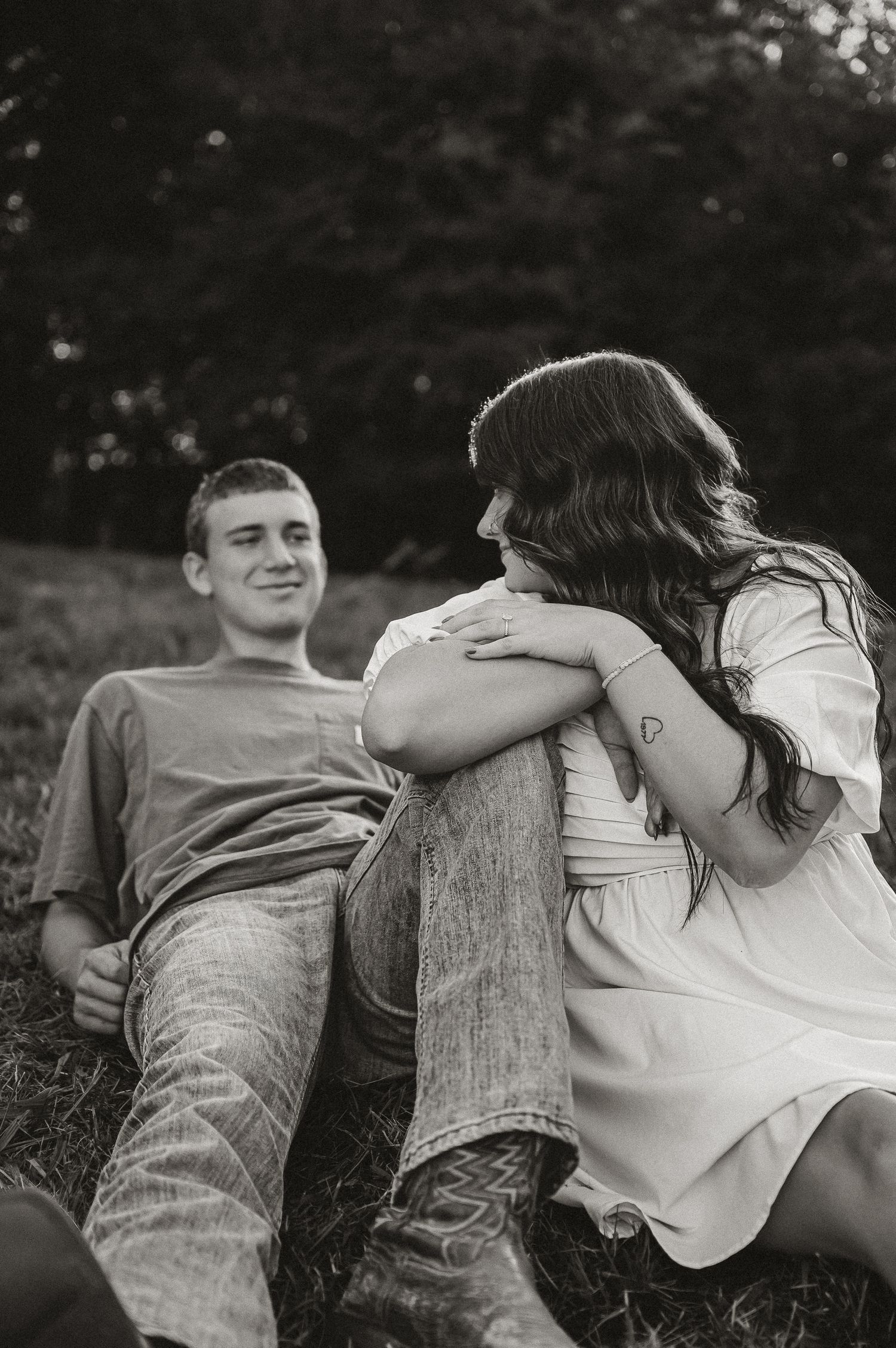 A casual couple relaxes together against a fallen tree trunk in a rustic outdoor setting.