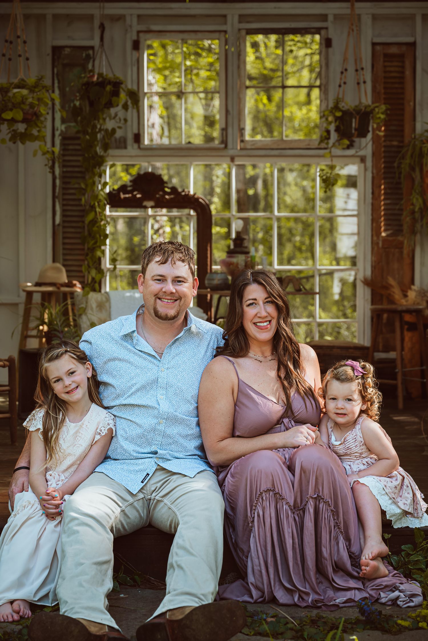 Family portrait session in casual attire sitting together on rustic wooden porch with natural lighting.