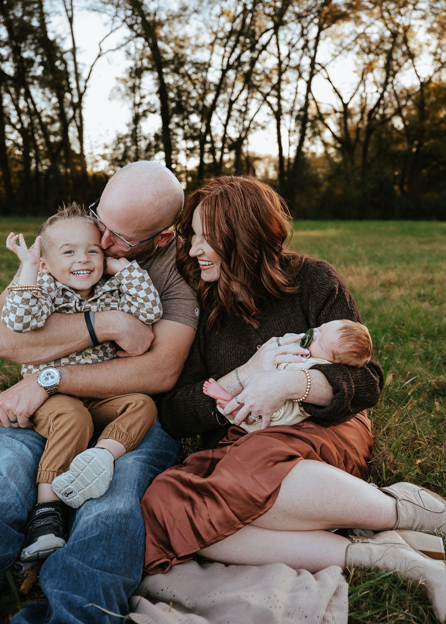 Loving family relaxes together on a blanket in a sunlit field during golden hour.