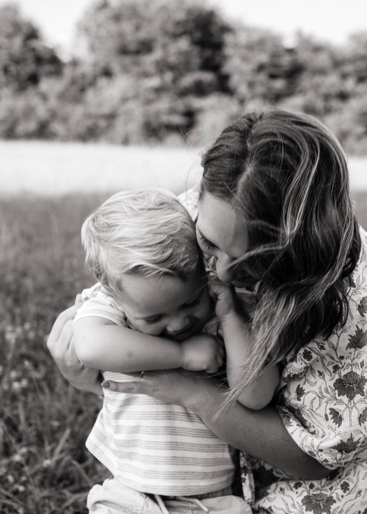 Black and white photo of a young mother lovingly embracing and kissing her toddler child outdoors.