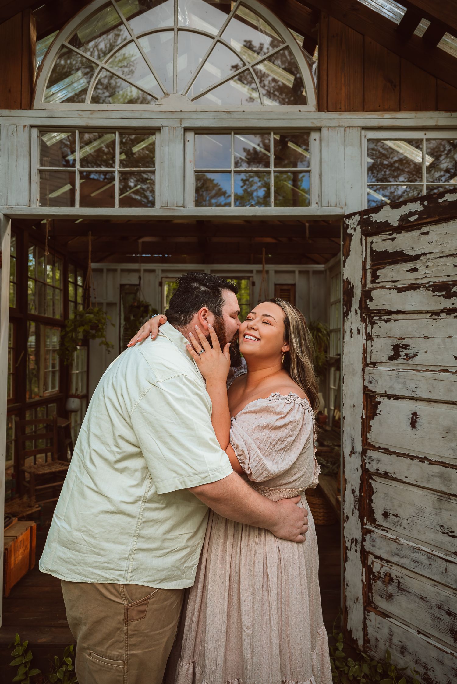 Couple sharing romantic moment in rustic white wooden building with arched windows.