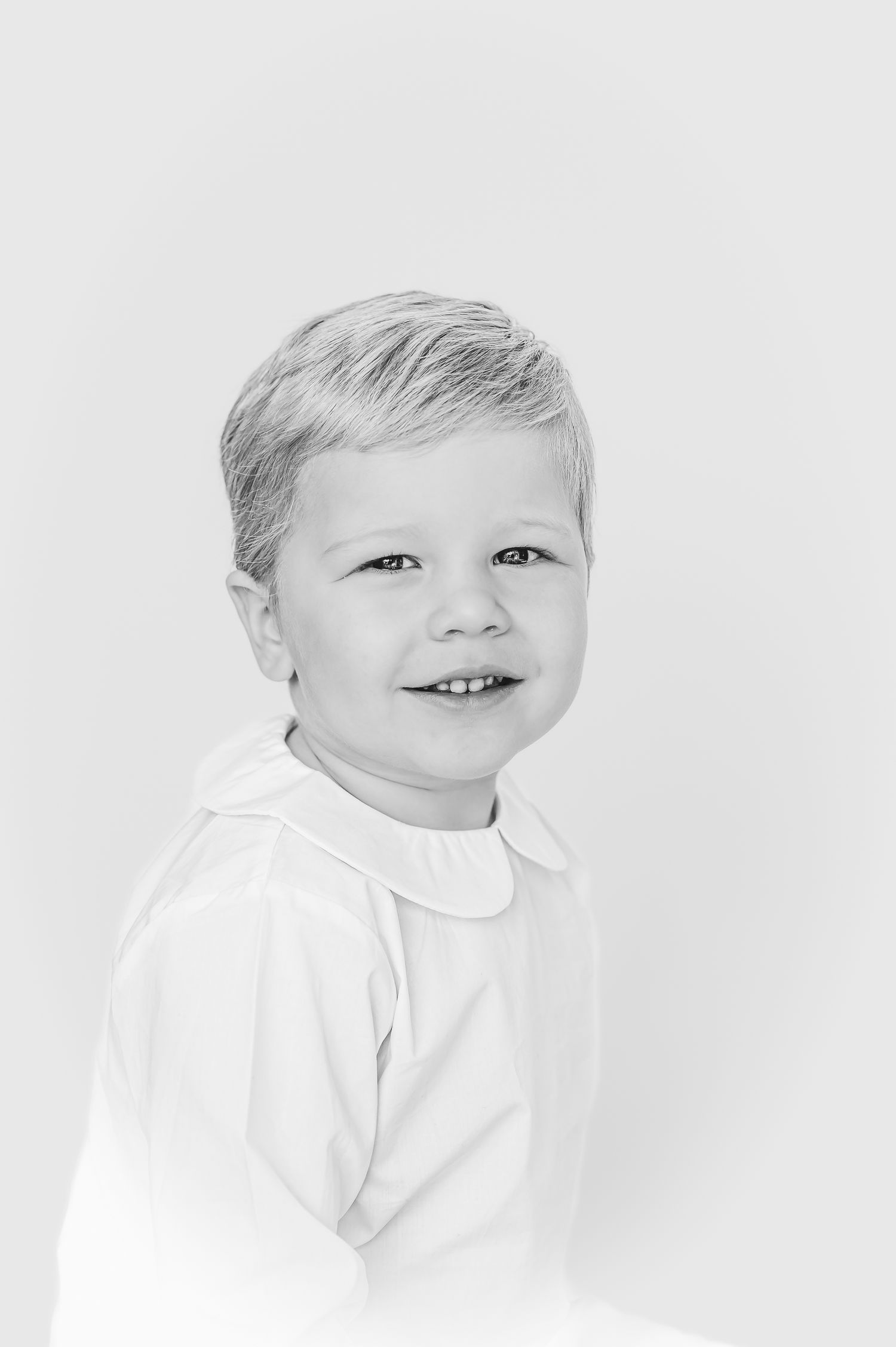 High key portrait of a child in white clothing against white background.