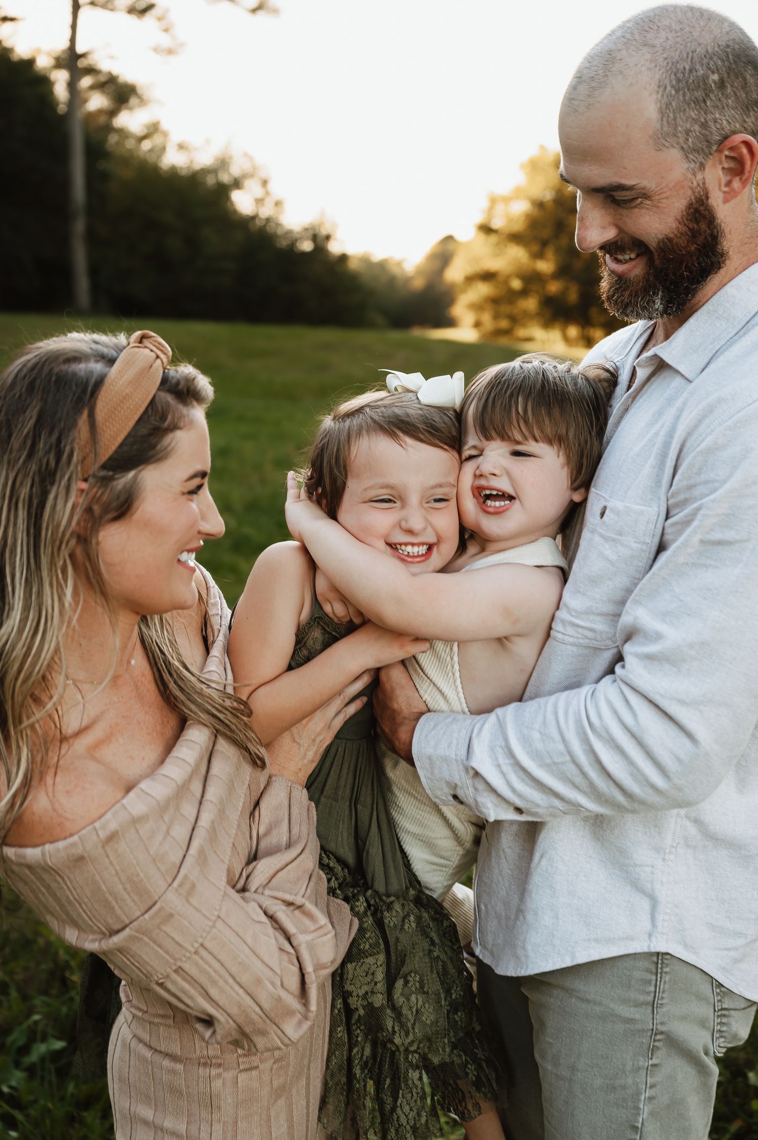 A joyful family shares laughter and embraces while posing against a tree at sunset.