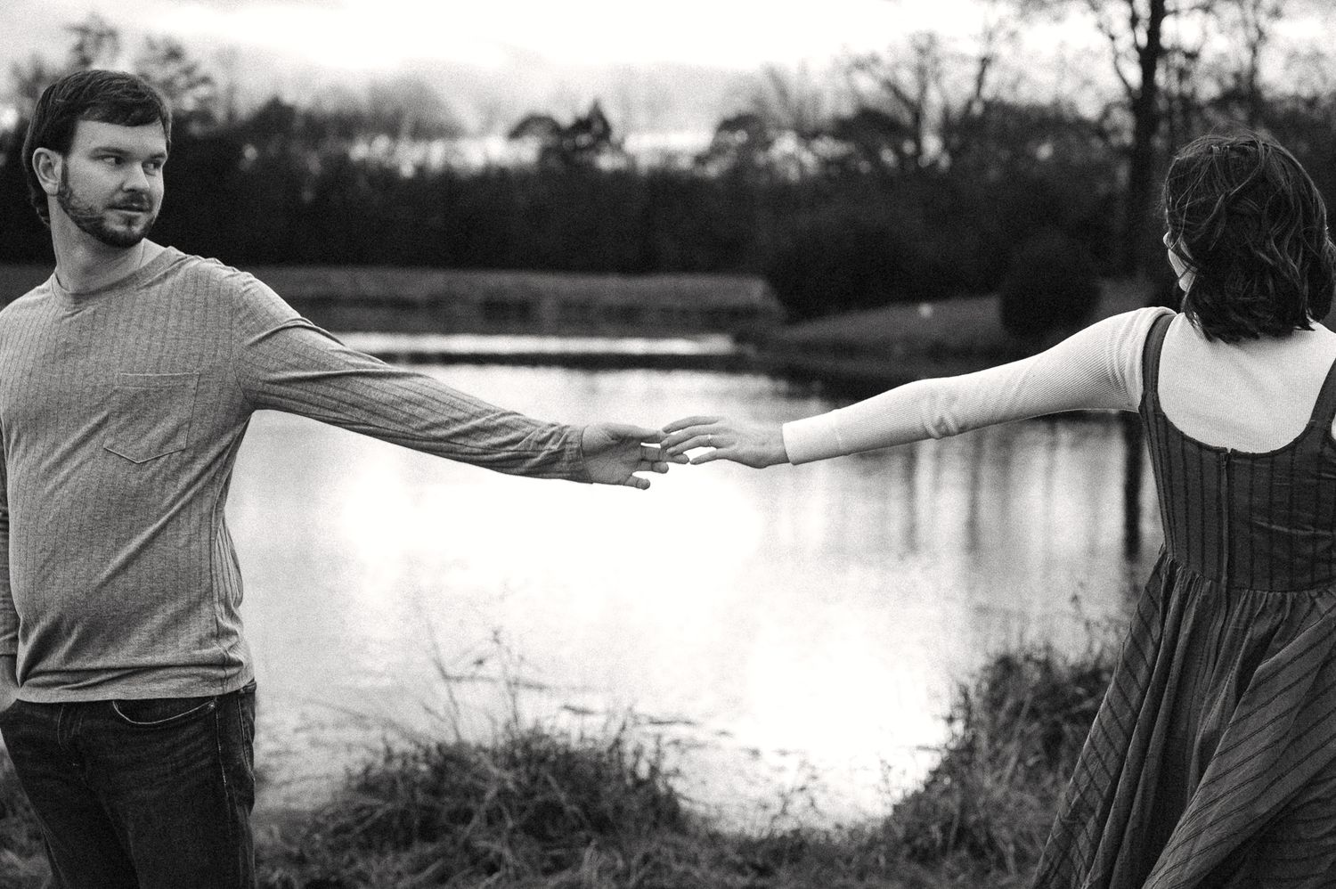 Silhouetted couple holding hands while walking along a serene waterfront at sunset.