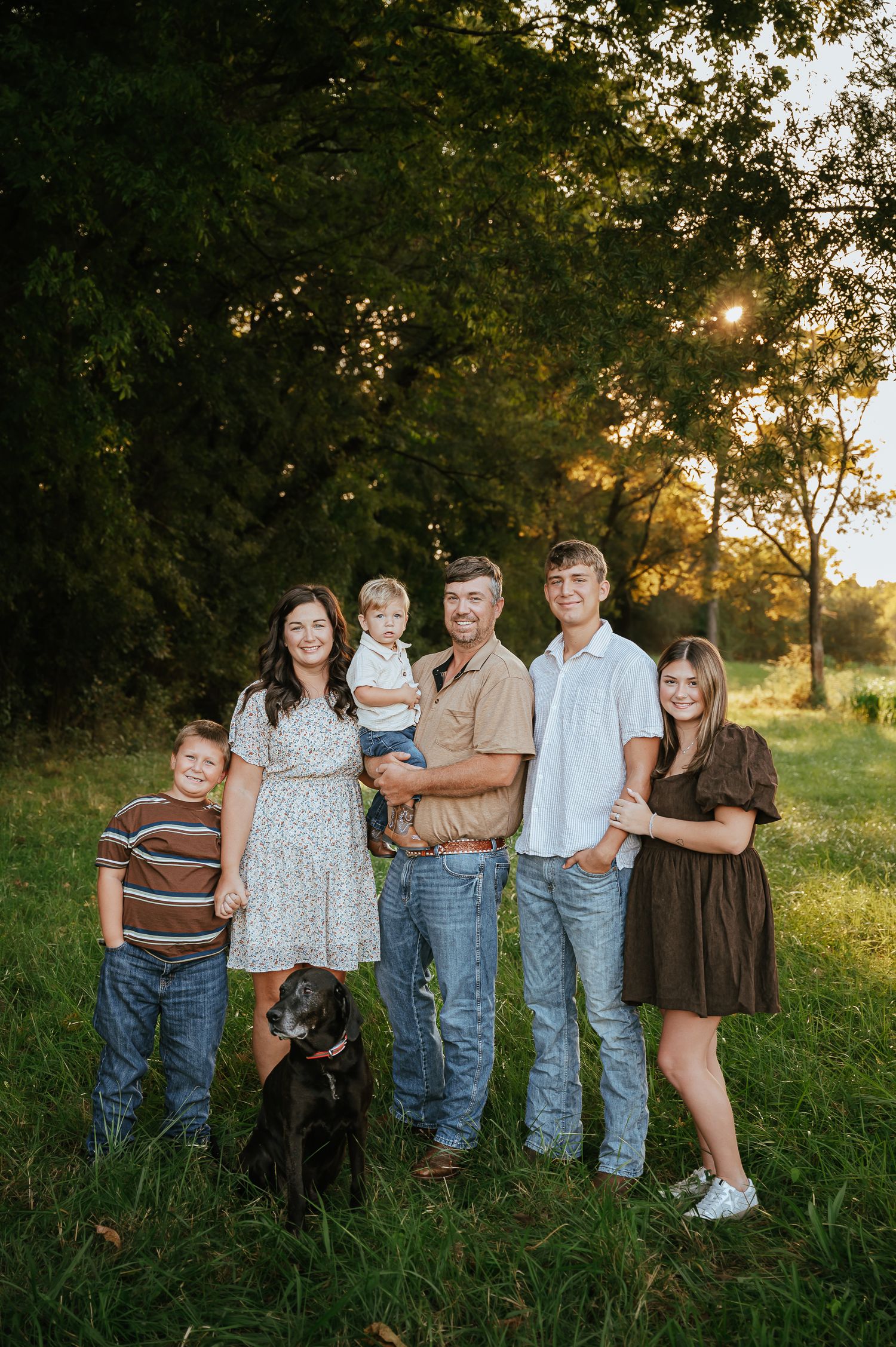 Family and their black dog pose together for portrait in golden evening light.